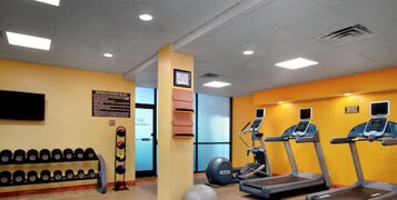 Un gimnasio con cintas de correr, una bicicleta estática y un estante de pesas.
