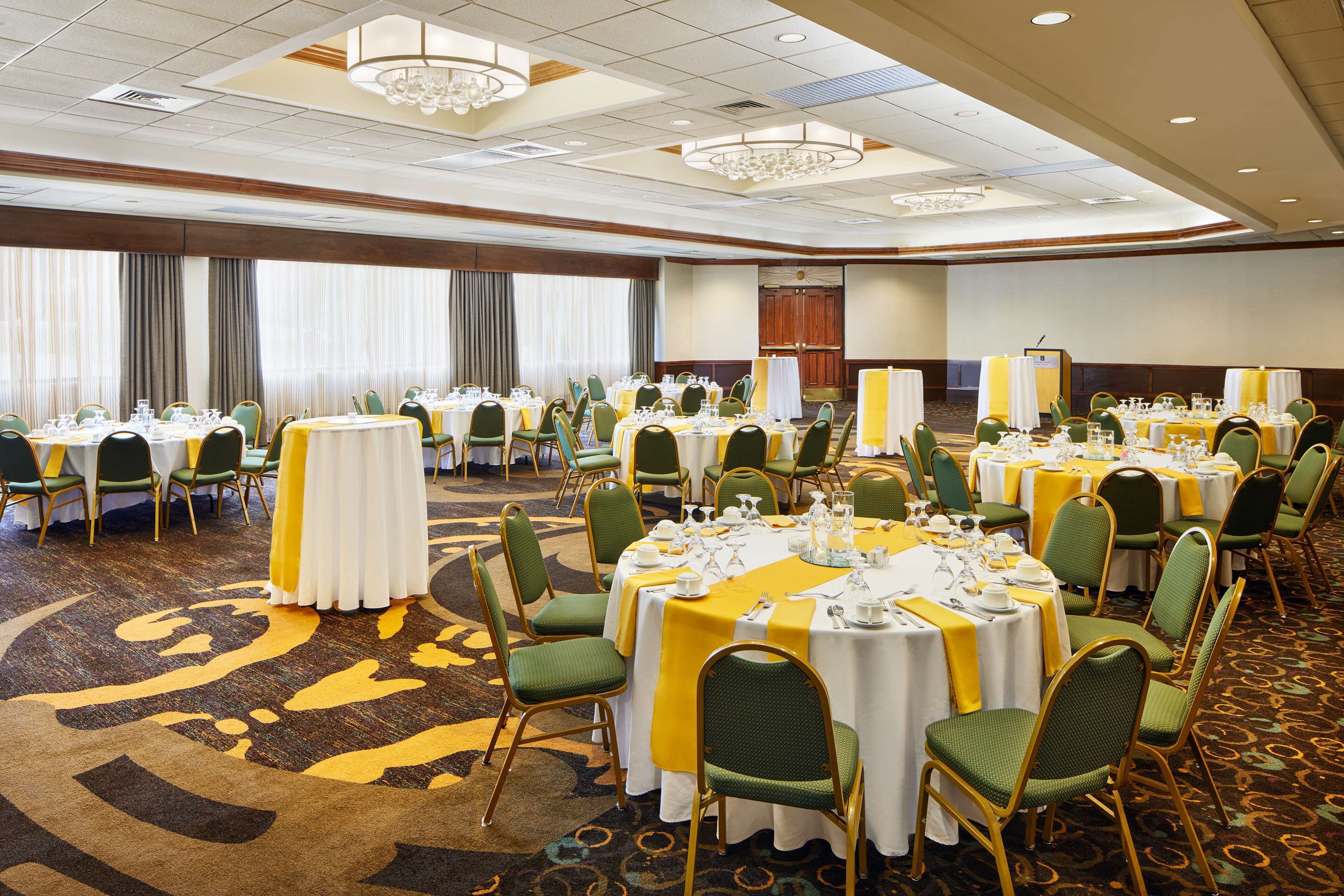 A banquet hall with round tables, green chairs, and yellow tablecloths.