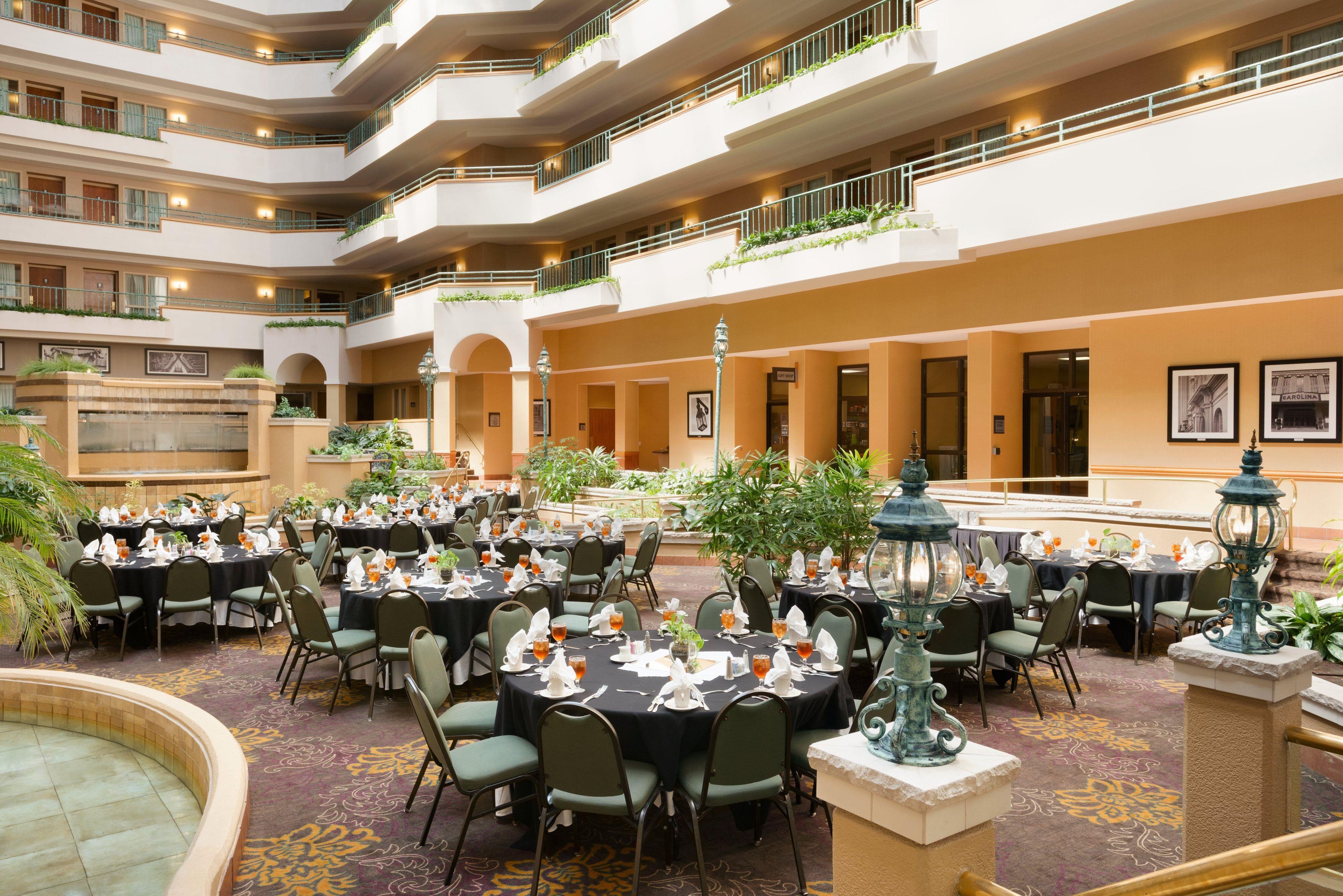 A multi-level dining area with tables set for guests, featuring a central fountain and surrounded by greenery.