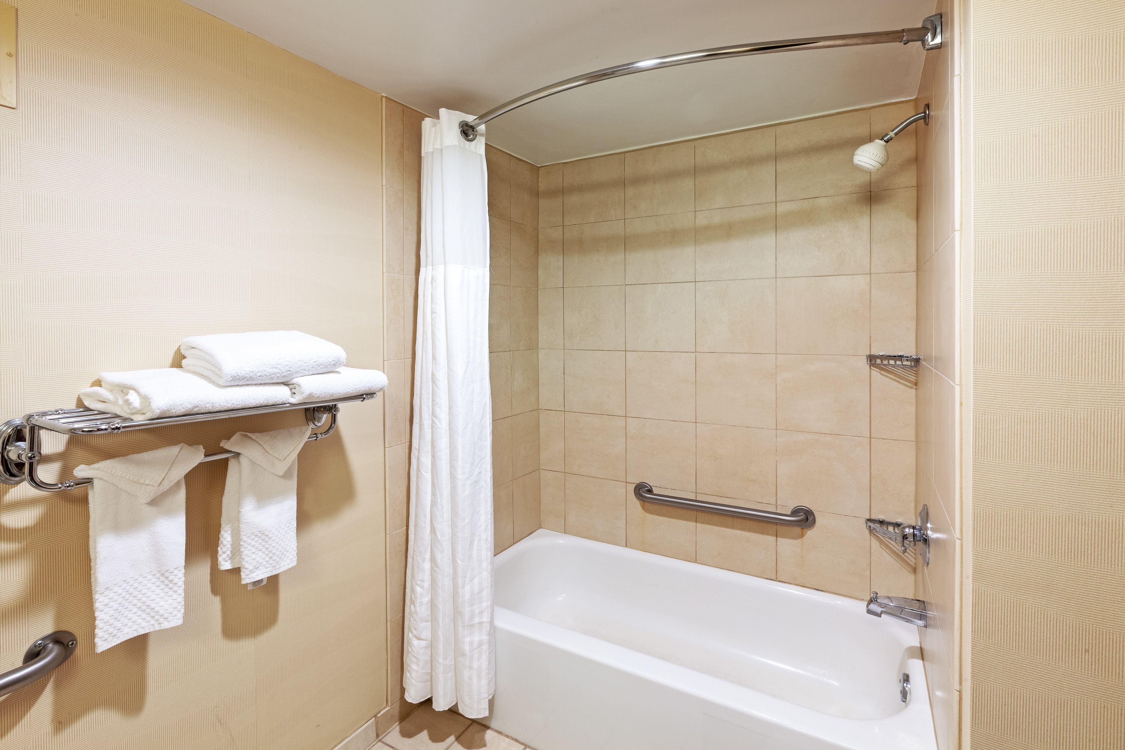 A bathroom with a bathtub, a shower curtain, and a towel rack with folded towels.