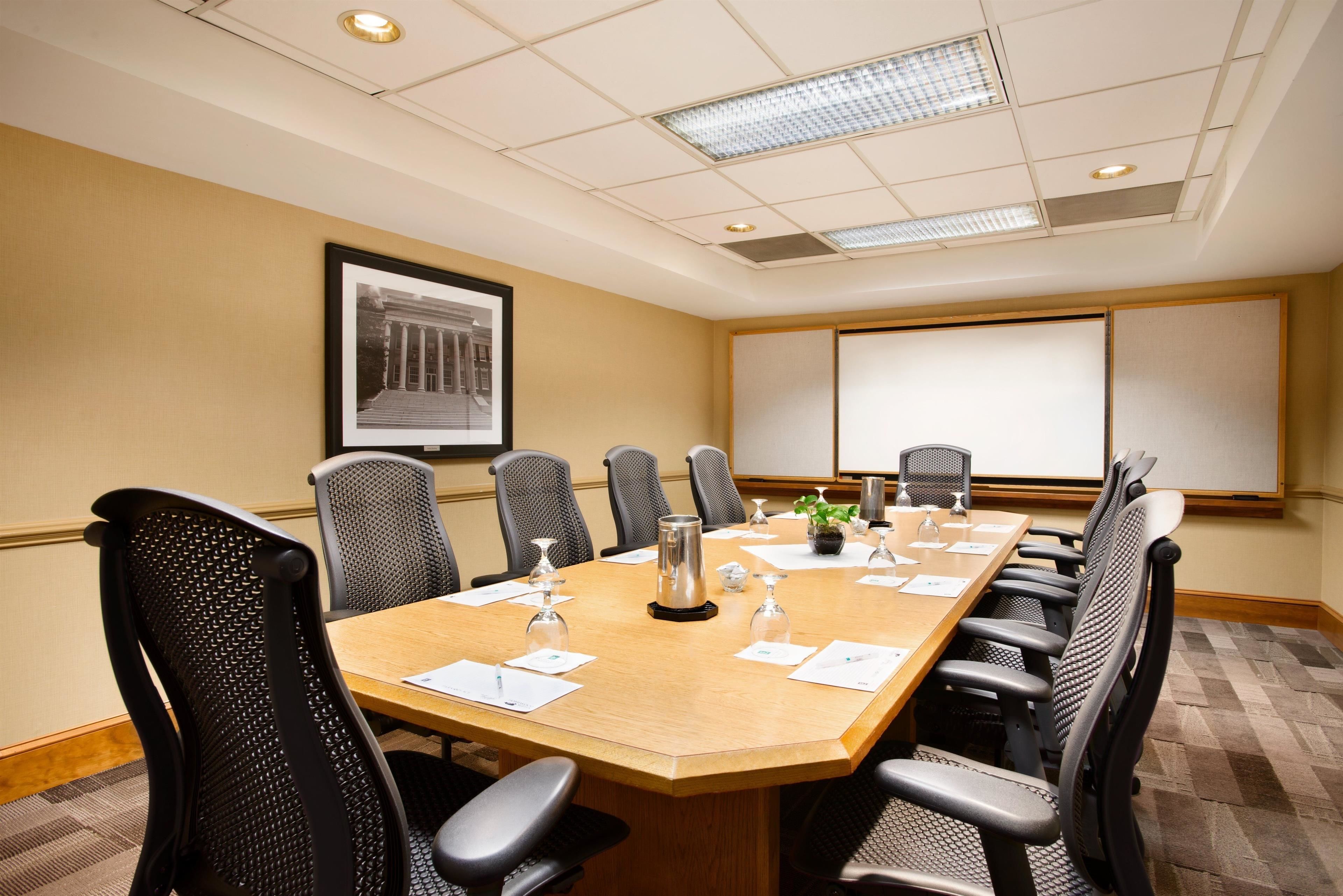 A conference room with a large table, chairs, a projector screen, and a framed picture on the wall.