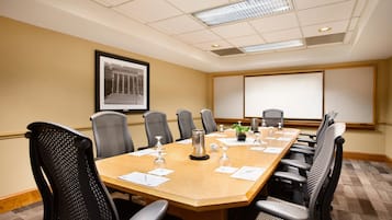 A conference room with a large table, chairs, a projector screen, and a framed picture on the wall.