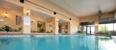 An indoor swimming pool with clear water, surrounded by beige walls, and equipped with wall-mounted lights.