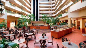 Un atrio de varios niveles con mesas y sillas para comer, una zona de bar central y varios balcones con plantas.