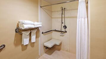 A bathroom with a shower, a grab bar, and a shelf with towels.