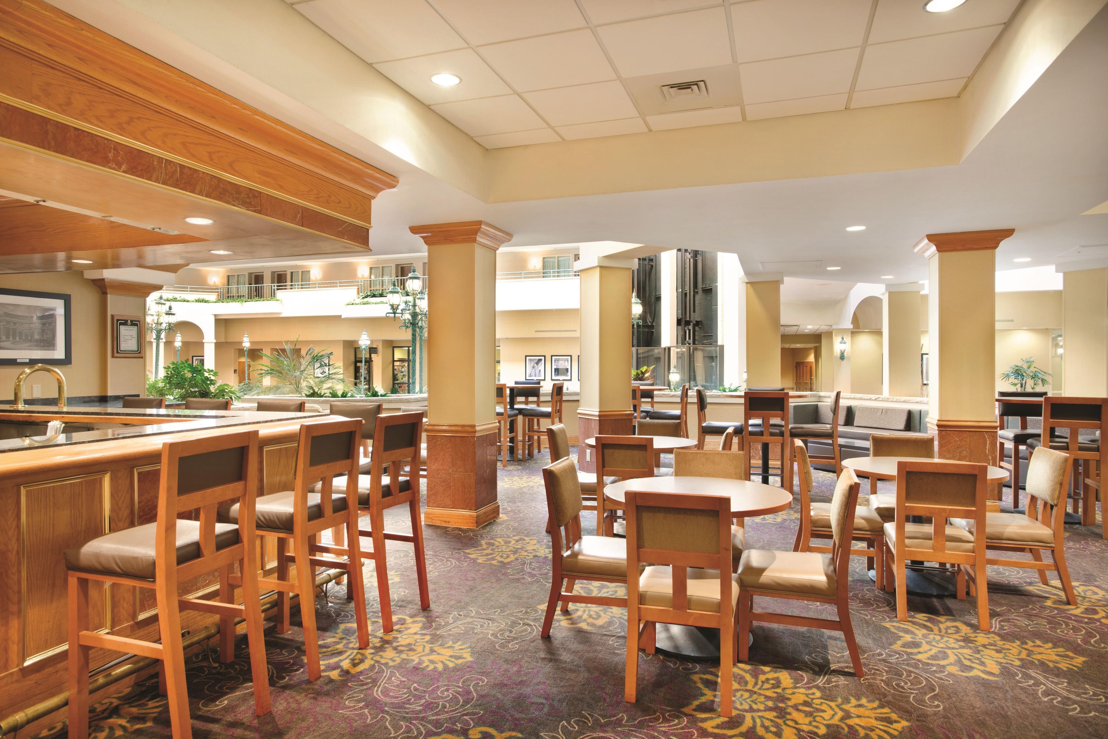 A hotel lobby with multiple seating areas, including a bar and dining tables.