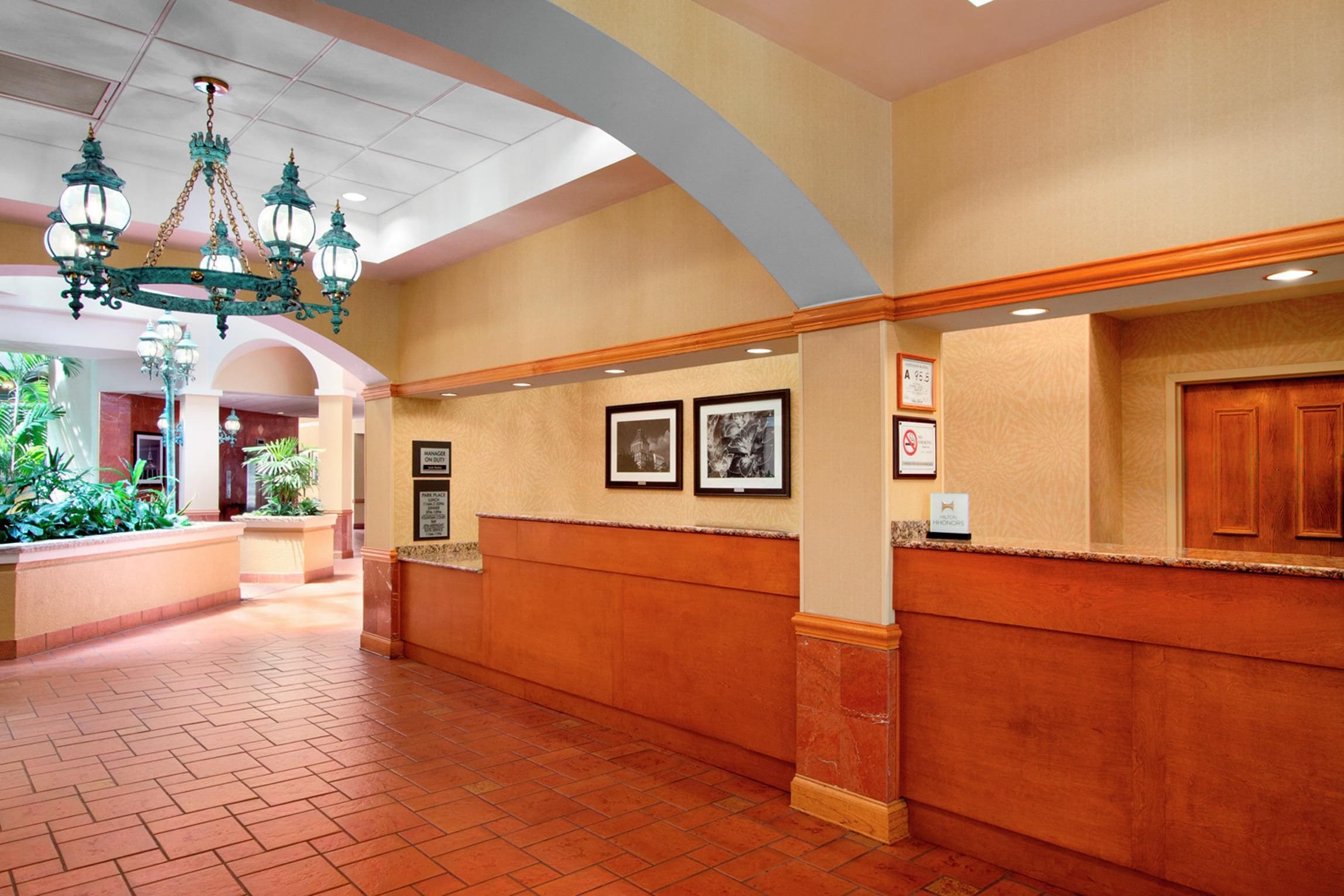 A hotel reception area with a marble floor, a chandelier, framed pictures on the wall, and a wooden reception desk.