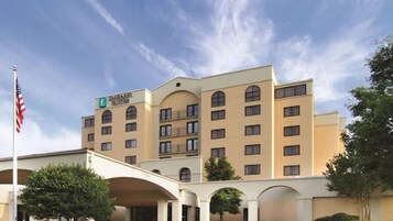 Un hotel de varios pisos con techo plano, una asta con la bandera estadounidense y un letrero que indica que es un hotel Marriott.