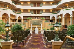 A hotel atrium with a central fountain, rows of chairs, and balconies with railings.
