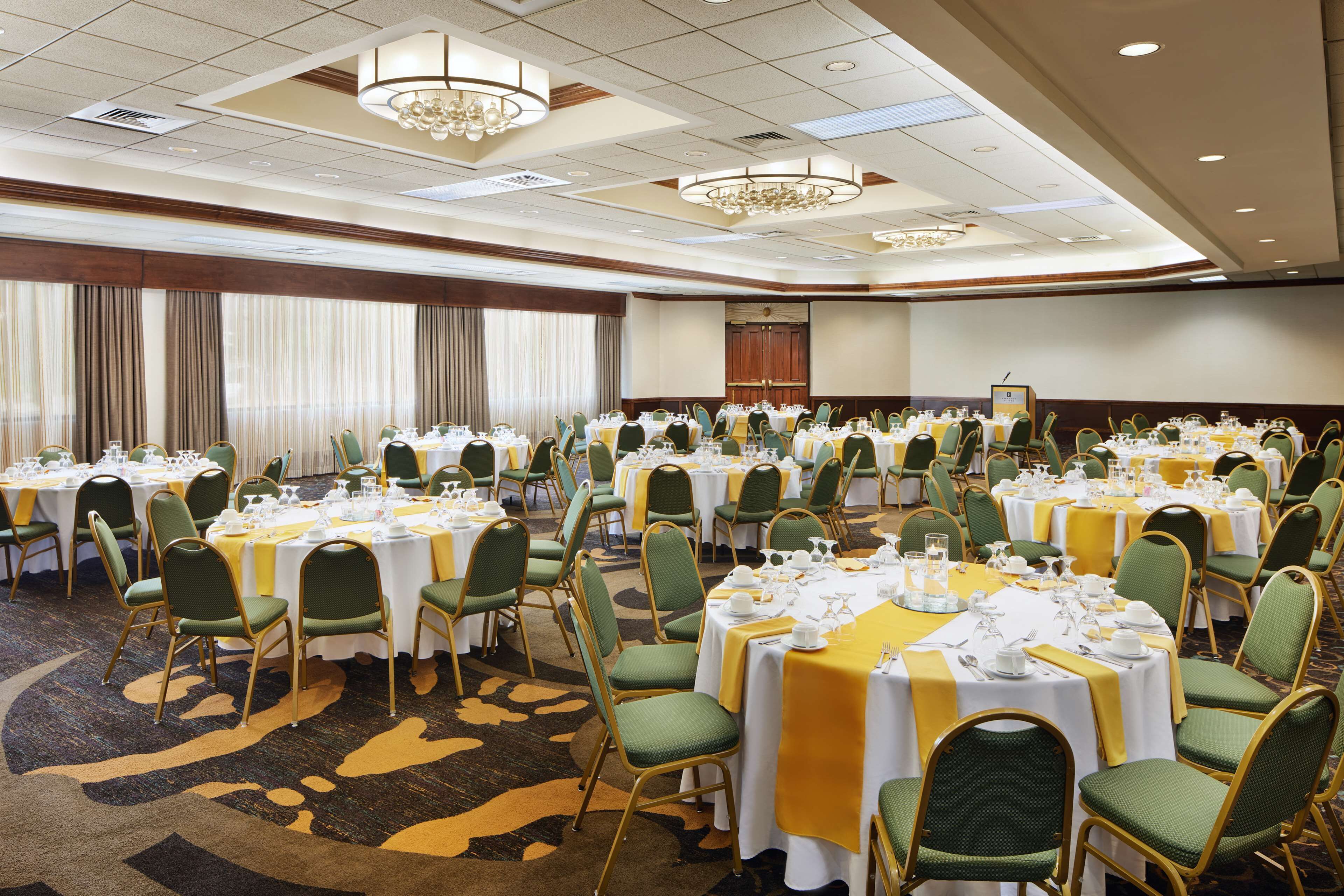 Un salón de banquetes con mesas redondas, sillas verdes y manteles amarillos.