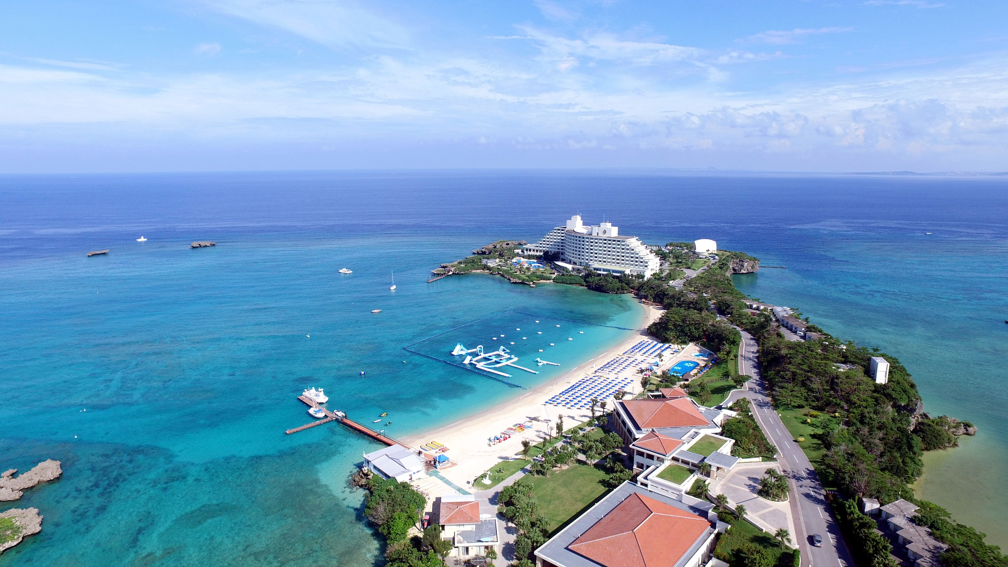 An aerial view of a coastal resort with a beachfront, a pier, and a large hotel.