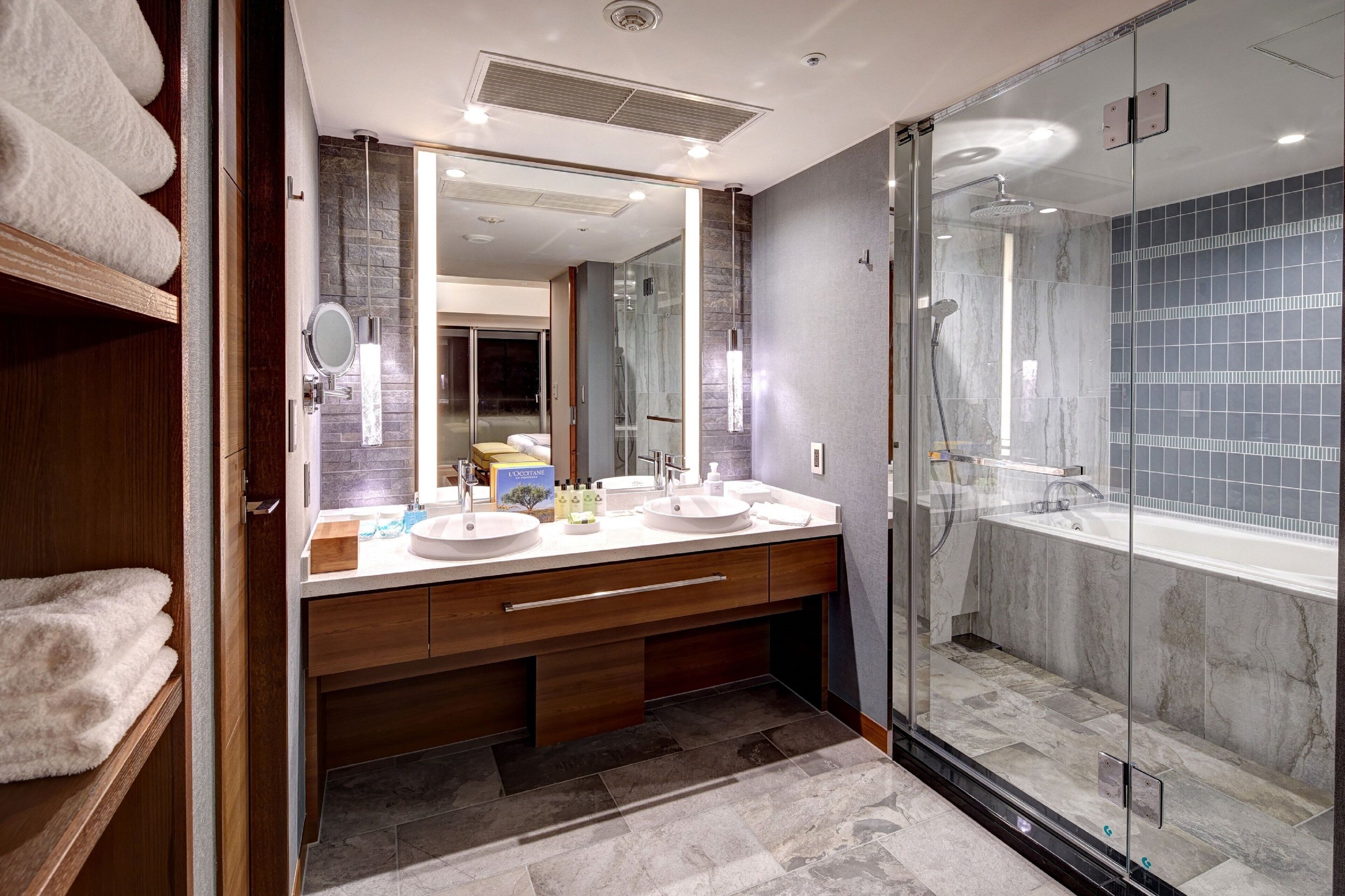 A modern bathroom with a glass-enclosed shower, two sinks, and a vanity with a mirror.