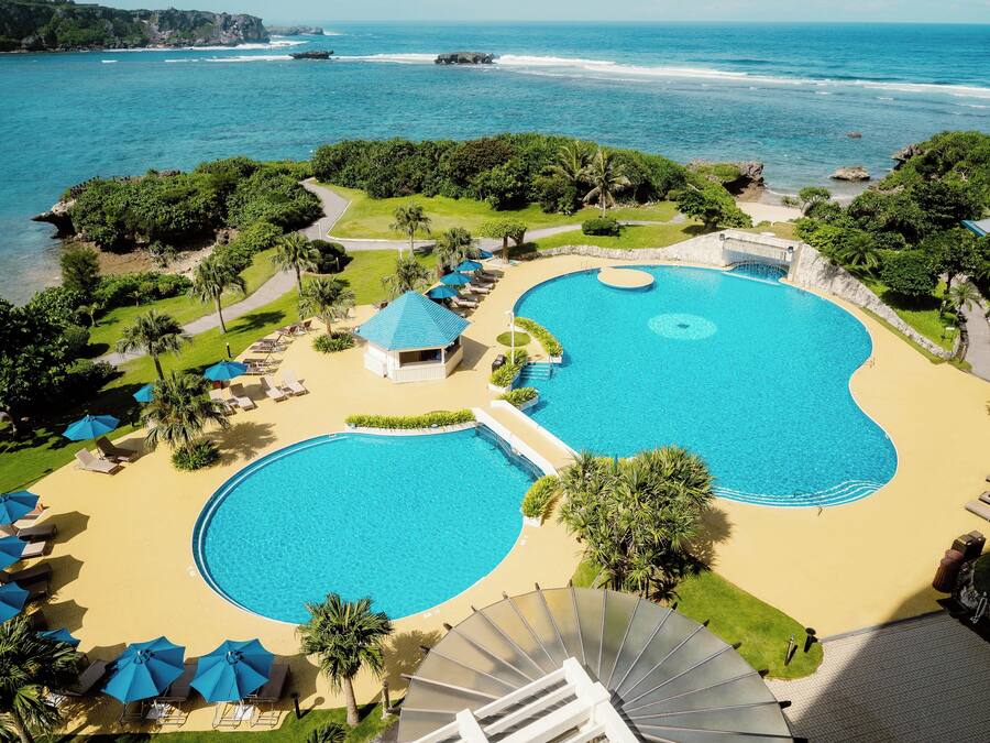 A resort with two large swimming pools, a beach area, and a view of the ocean.