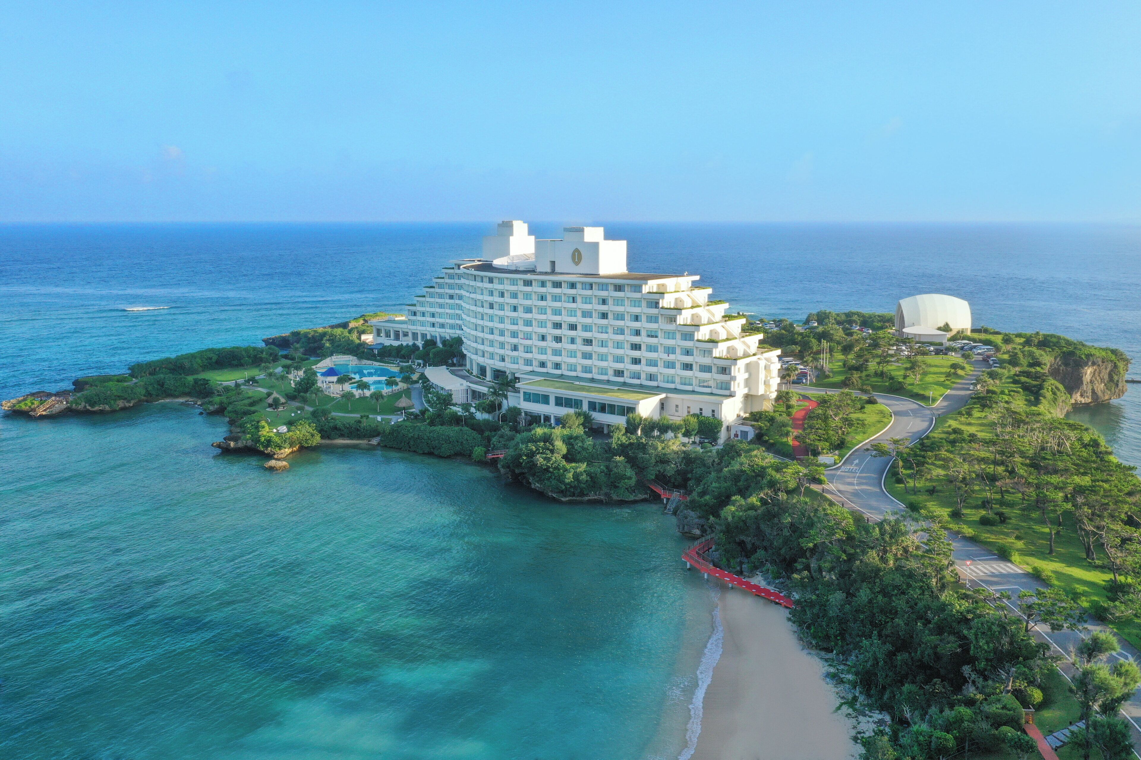 A large resort hotel with multiple buildings, a swimming pool, and a beach.