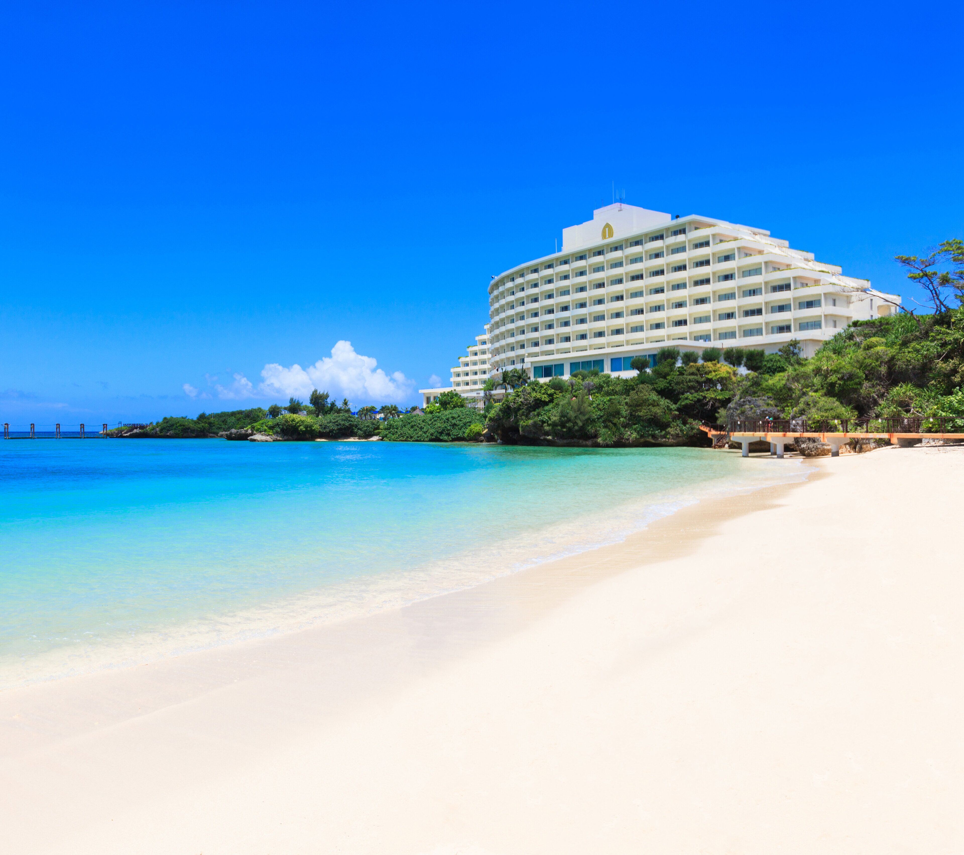 A beachfront hotel with a large building, a sandy beach, and clear blue water.