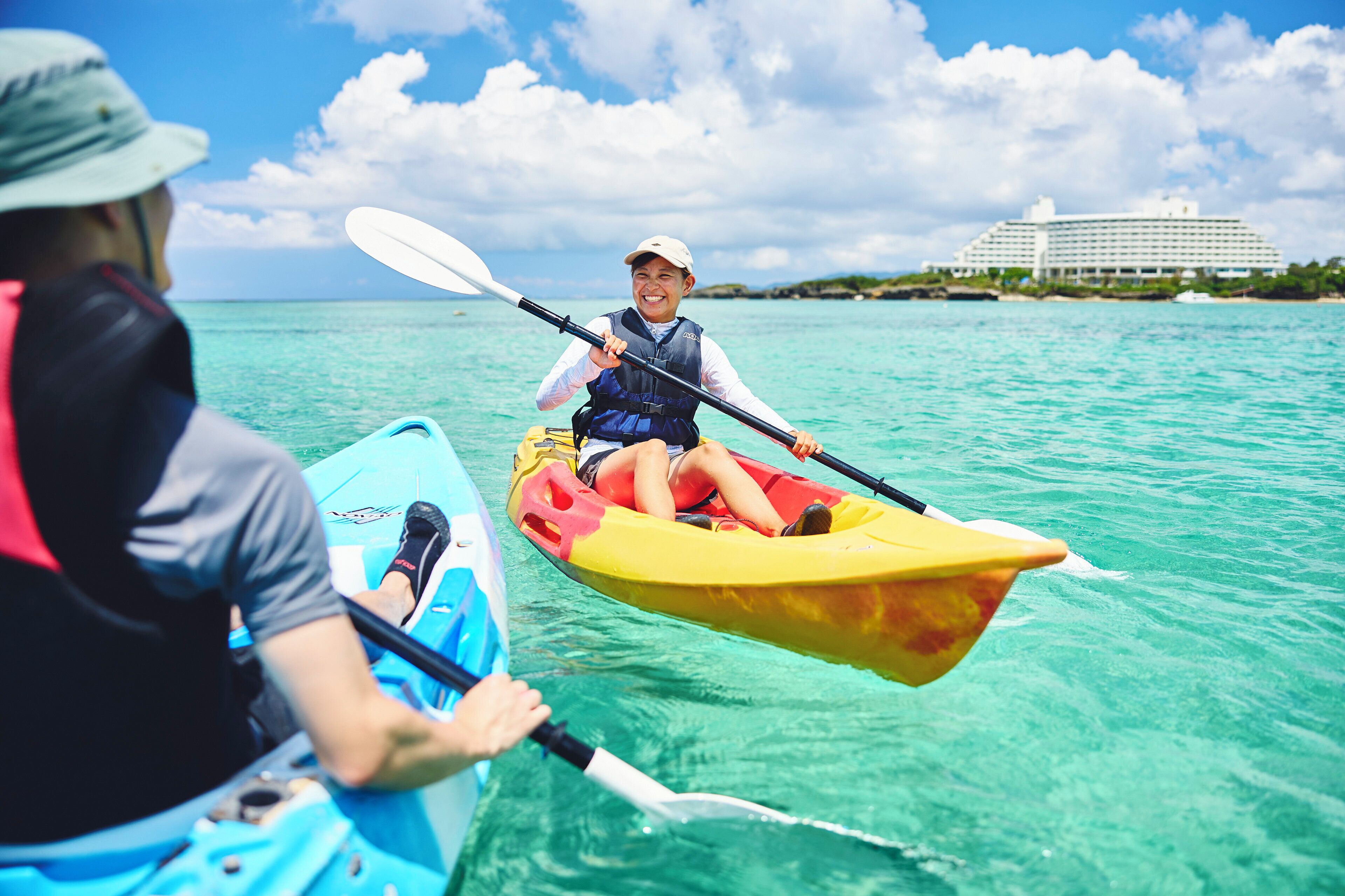 Dos personas hacen kayak en aguas turquesas, con un edificio de resort al fondo.