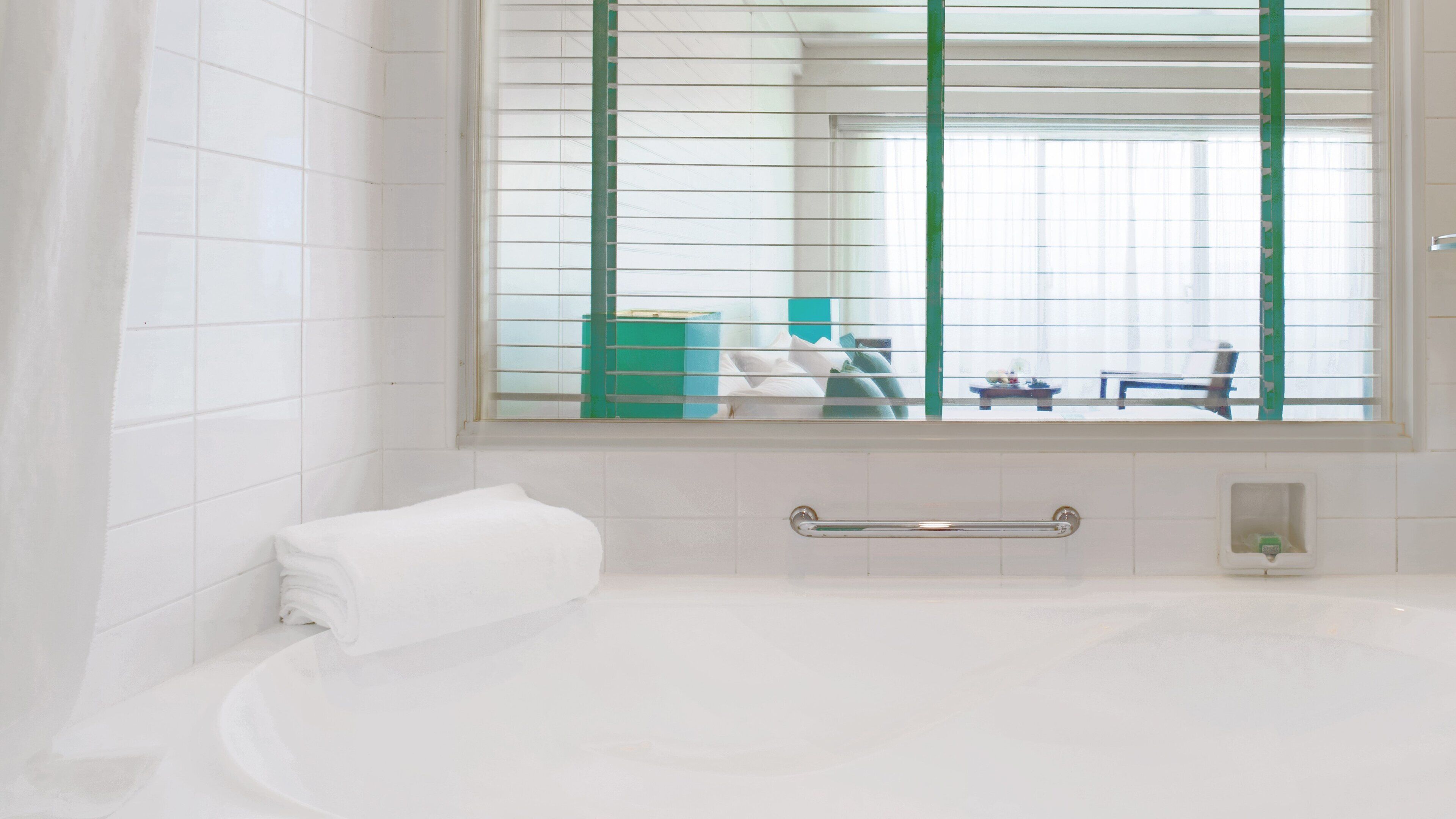 Une salle de bain moderne avec une grande baignoire, un miroir et une fenêtre équipée de stores.