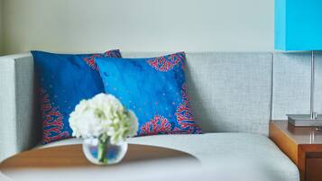 A modern living room with a light grey sofa, a blue patterned pillow, a small white flower vase, and a blue lamp on a wooden side table.