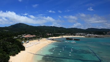 A beach with clear turquoise waters, a pier, and a mountainous backdrop.