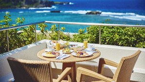 A dining table with breakfast items and a glass of orange juice, overlooking a coastal view with the ocean and rocky outcrops. - ANA InterContinental Manza Beach Resort by IHG (Onna)