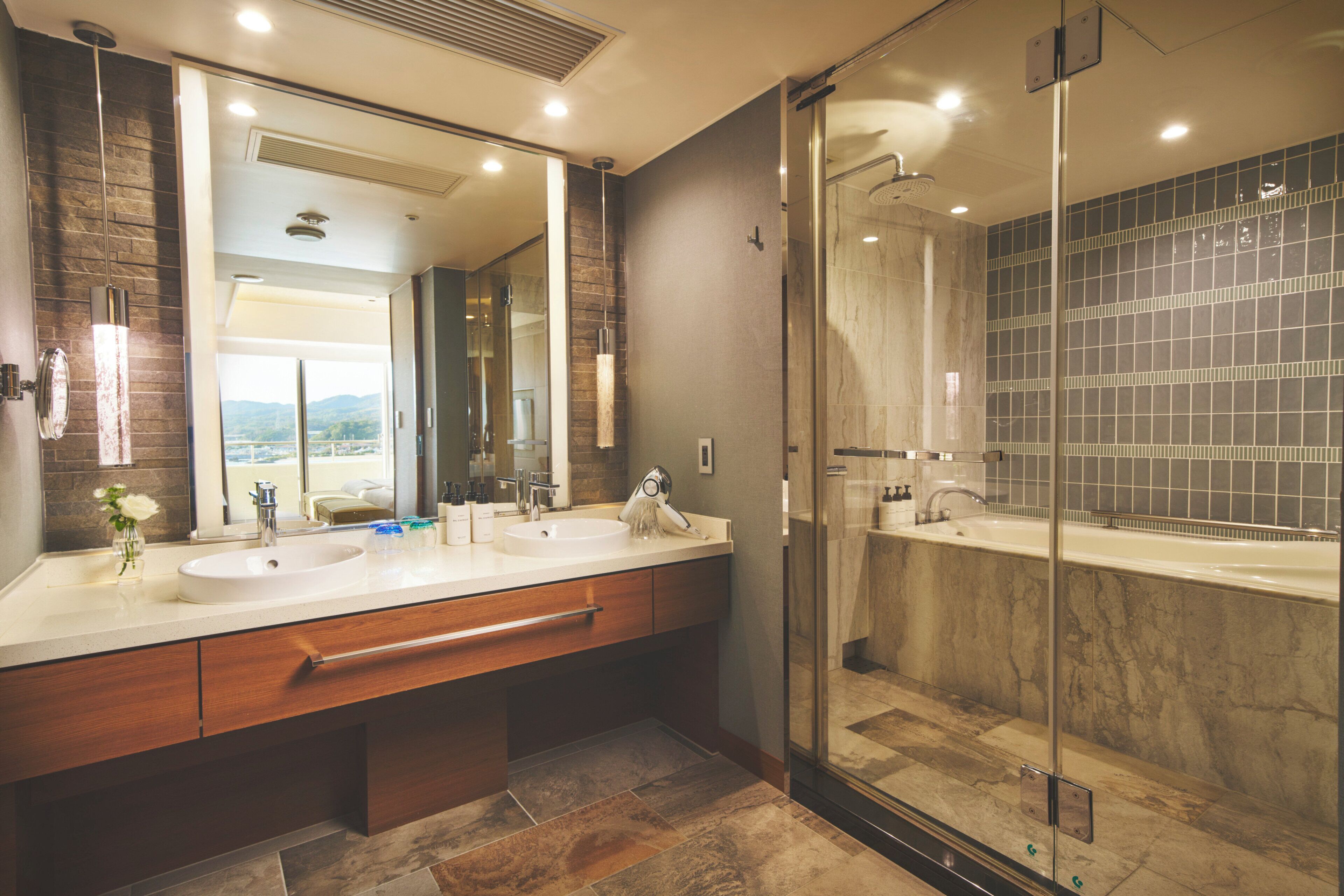 A modern bathroom with two sinks, a large mirror, and a glass-enclosed shower.