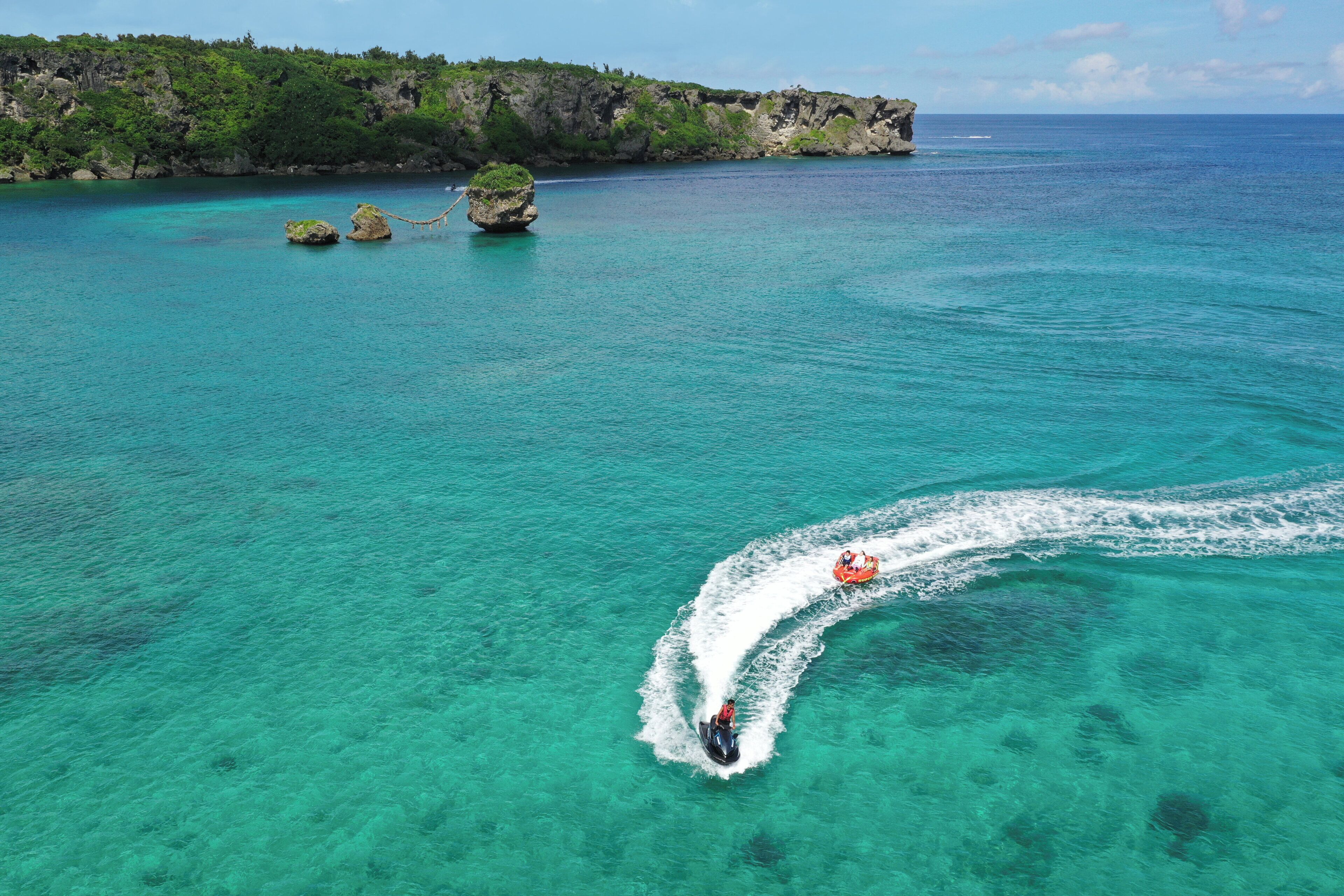 Une mer turquoise aux eaux limpides, traversée par un jet ski qui laisse derrière lui une vague.