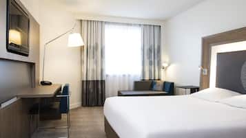 Habitación de hotel con cama, escritorio, silla, lámpara y ventana con cortinas.