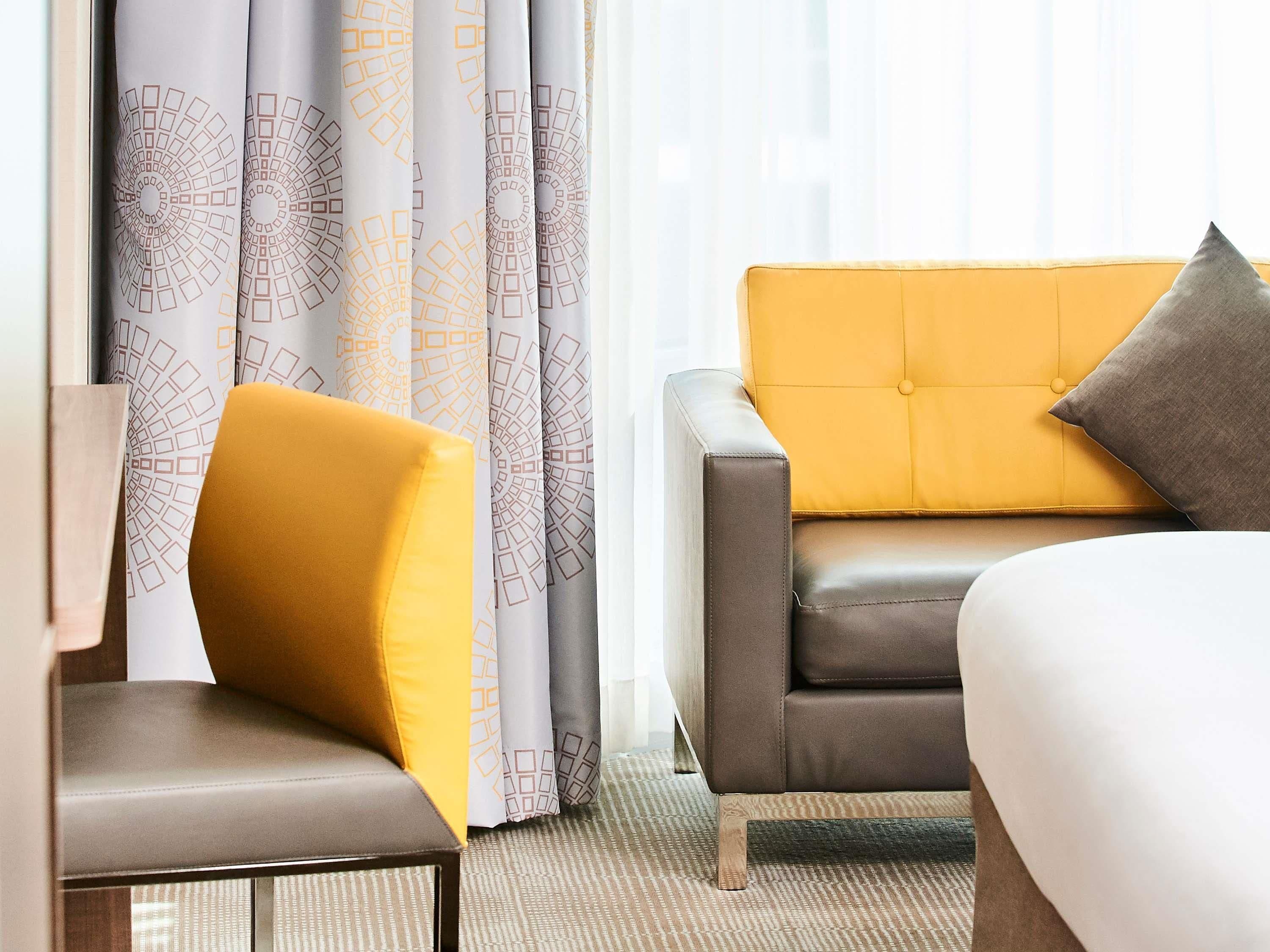 A hotel room with a sofa, armchair, and curtains with geometric patterns.
