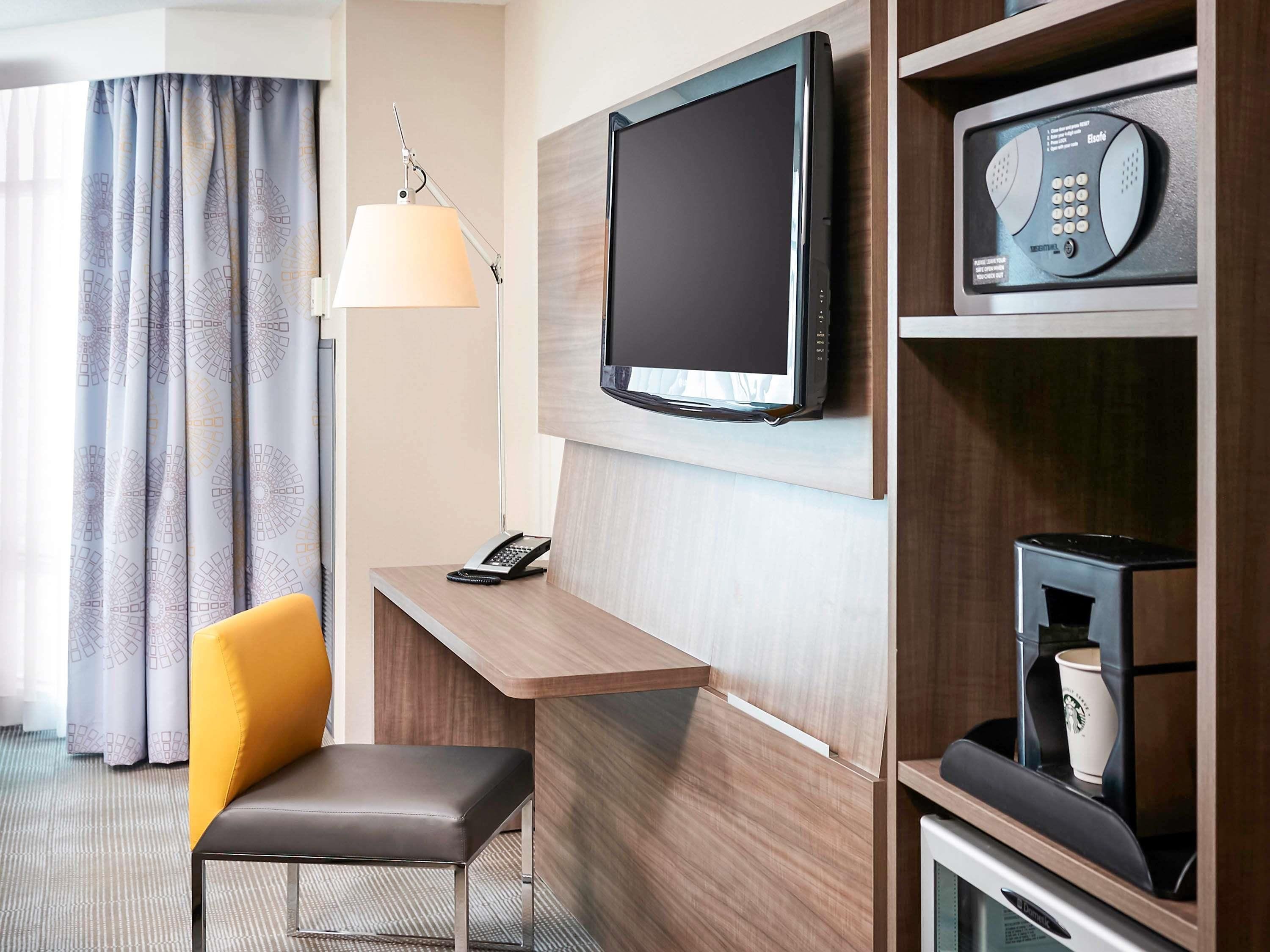 Una habitación de hotel con escritorio, silla, televisor, teléfono y cafetera.