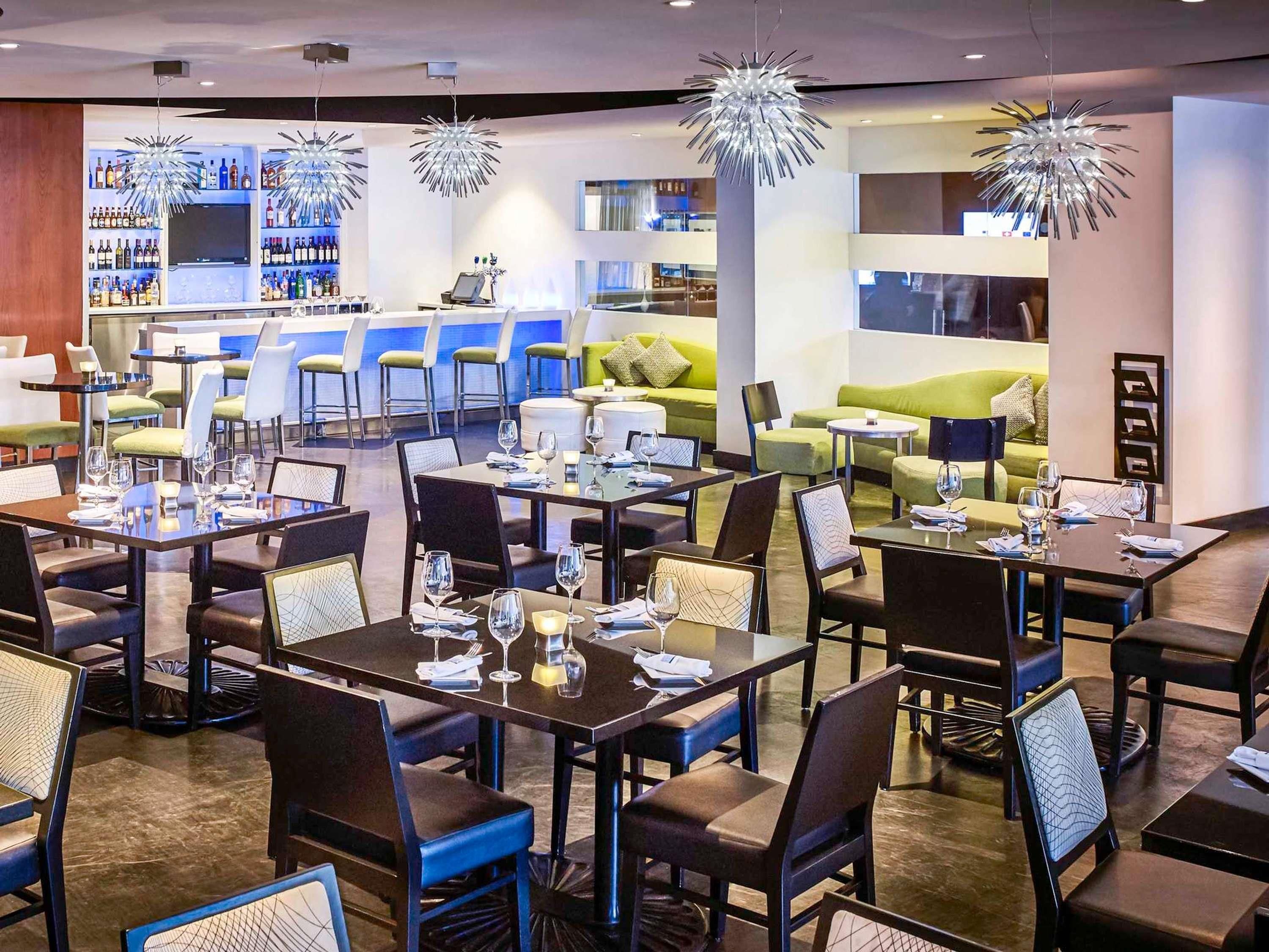 Un restaurante moderno con mesas y sillas, una zona de bar y un área de estar con un sofá verde.