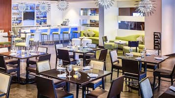 Um restaurante moderno com mesas, cadeiras, um bar e uma área de estar com um sofá verde.