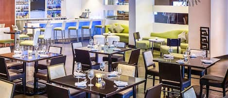 Un restaurante moderno con mesas y sillas, una zona de bar y un área de estar con un sofá verde.