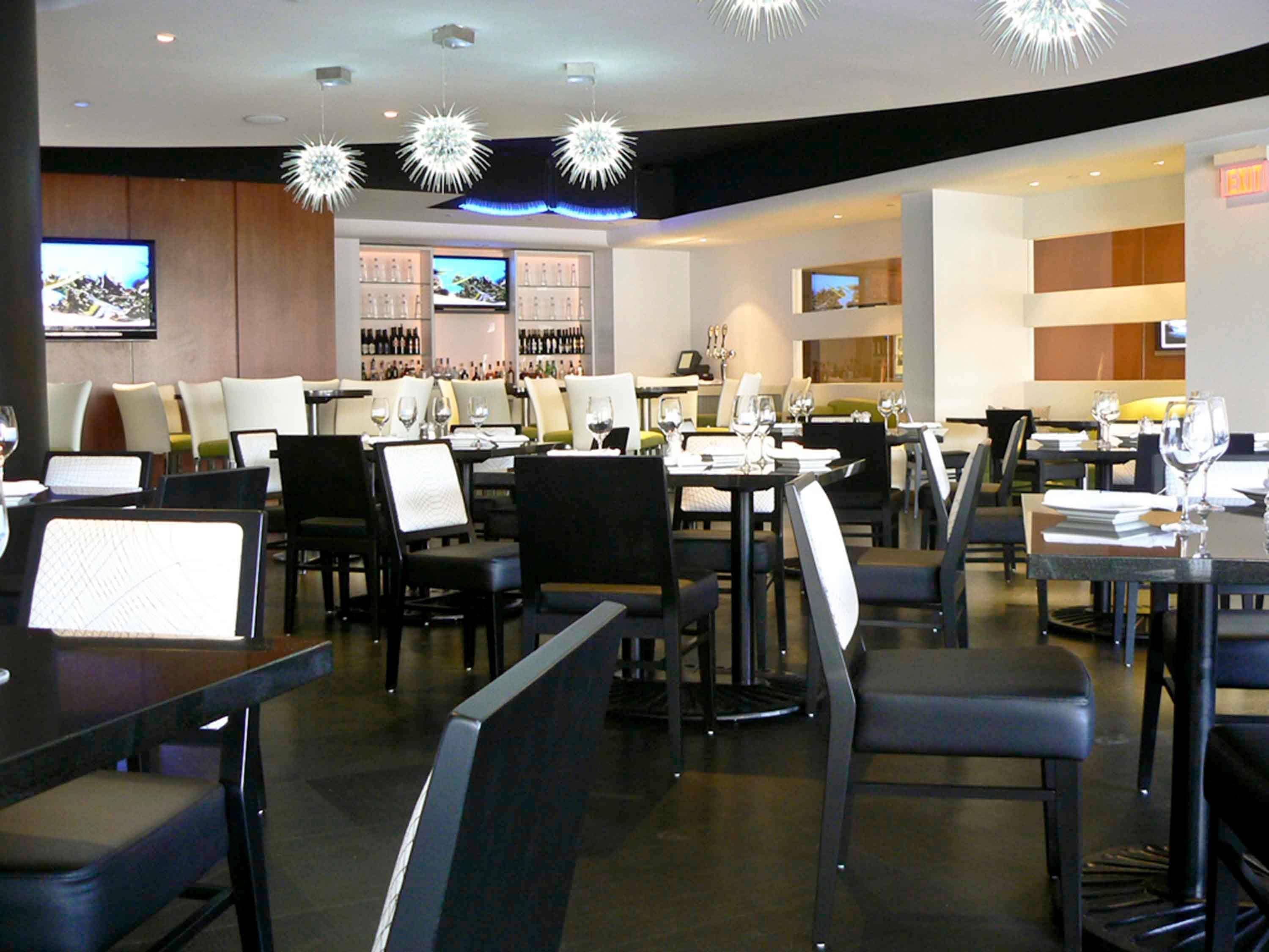Un restaurante moderno con varias mesas y sillas, una zona de bar con botellas, y una pantalla de televisión.
