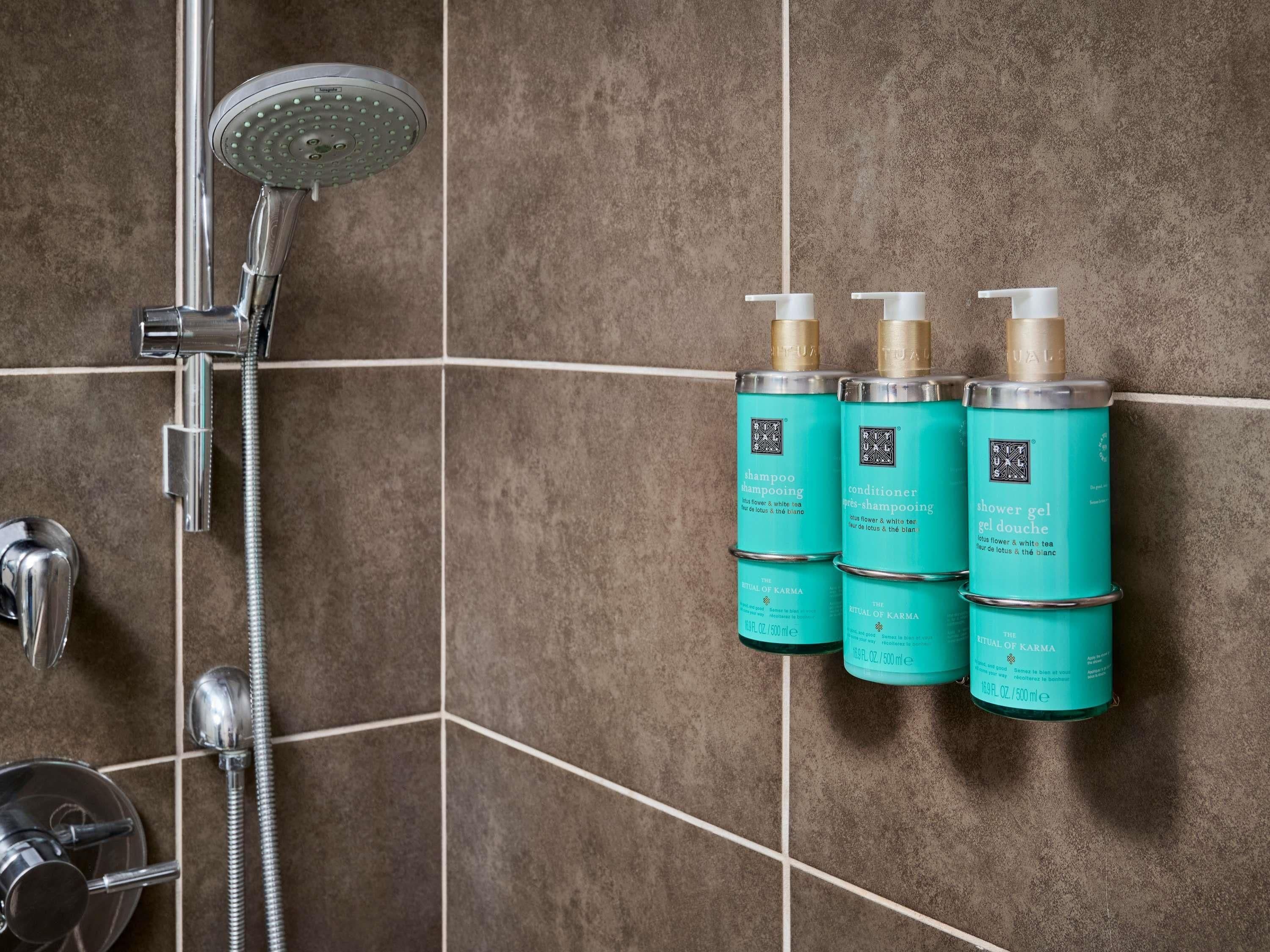 Un baño con ducha, cabezal de ducha manual y tres botellas de champú y acondicionador en una pared de azulejos.