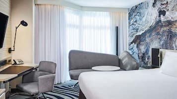 Een hotelkamer met een bed, twee fauteuils, een bureau met telefoon, een televisie en een groot raam met gordijnen.