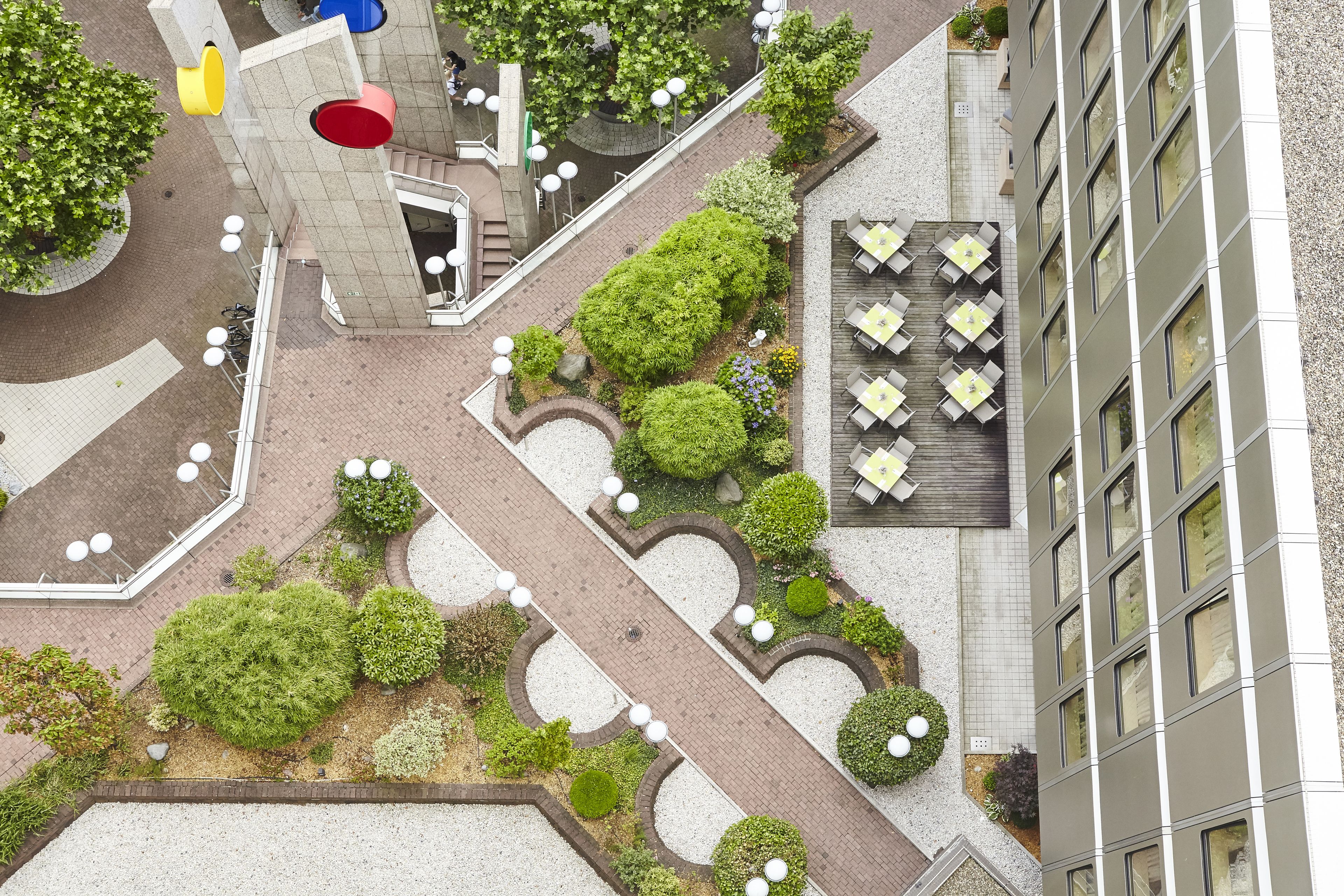 An aerial view of a hotel courtyard with a central pathway, surrounded by greenery and outdoor seating areas.