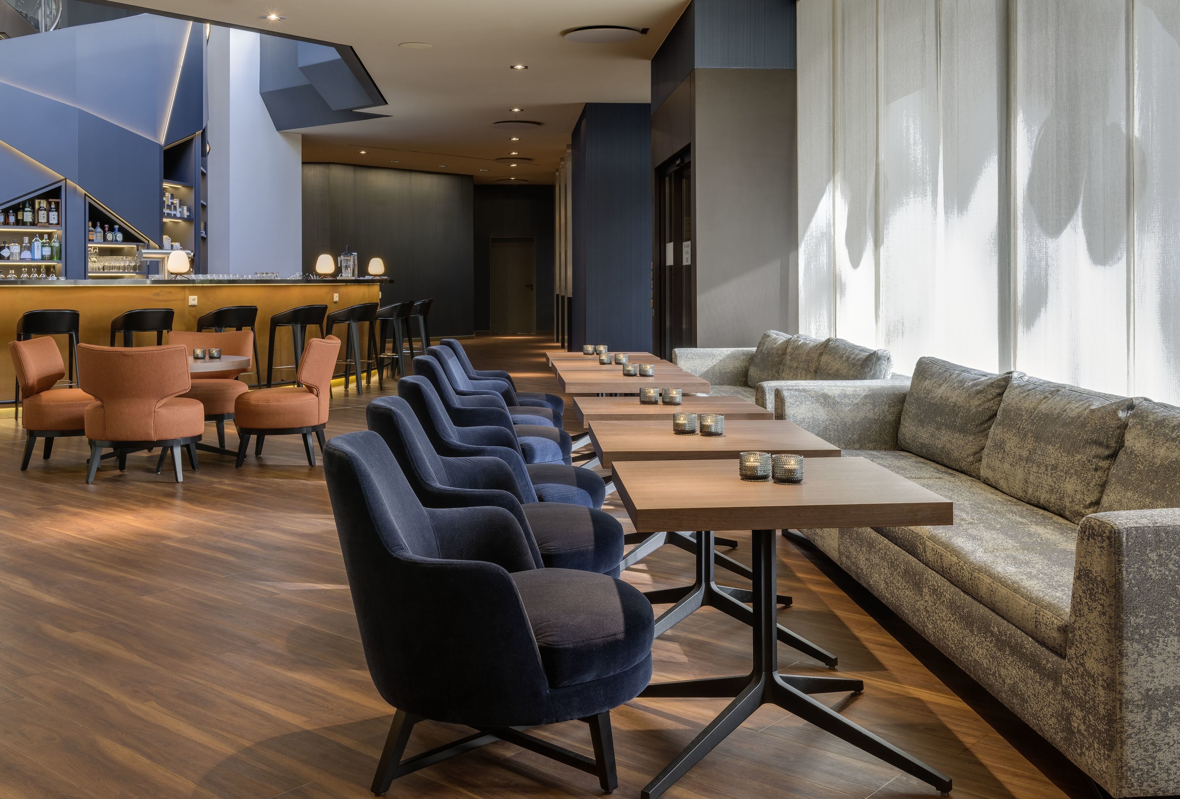 A modern lounge area with a bar, seating arrangements, and a large window providing natural light.