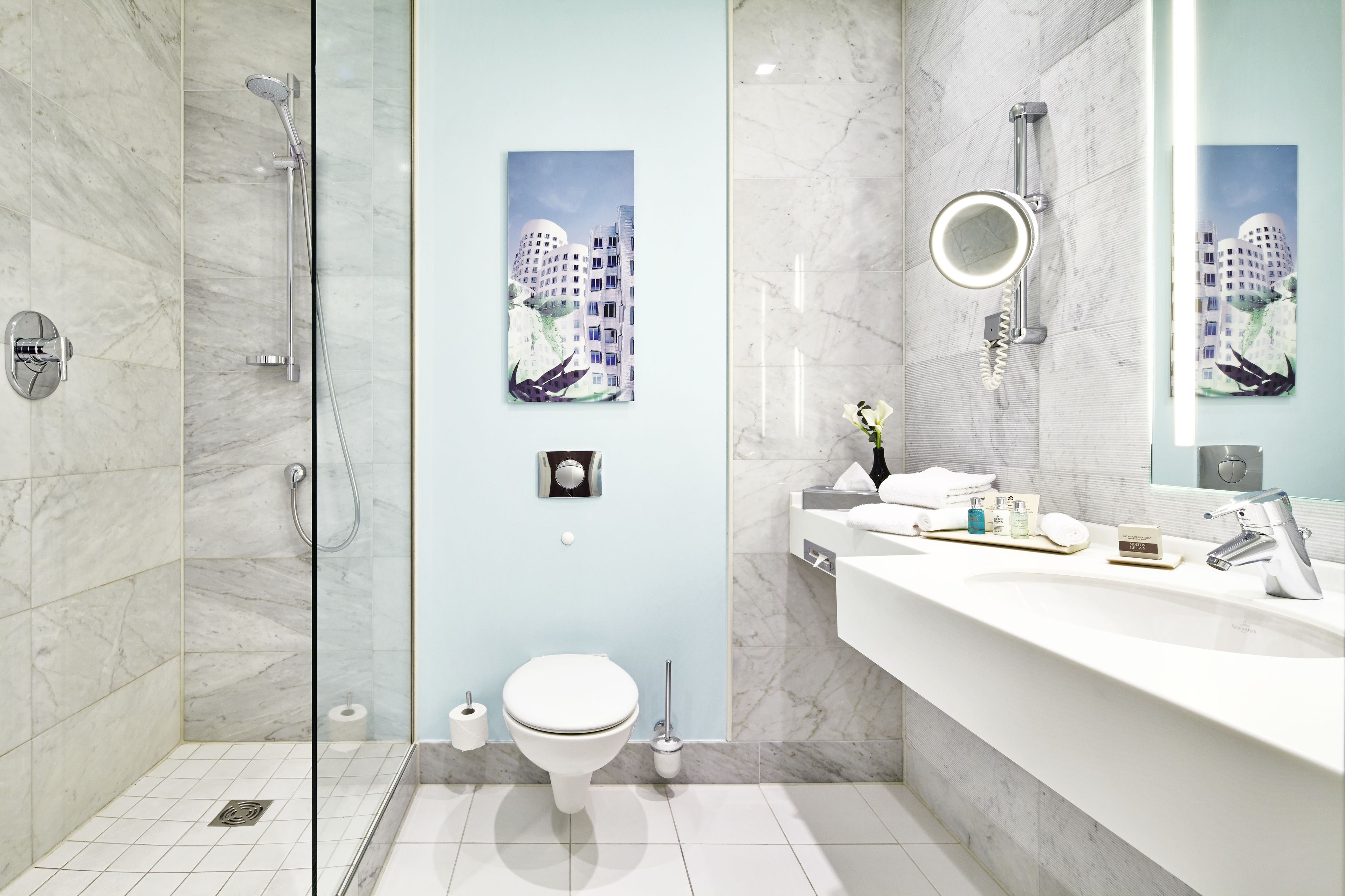 Un baño moderno con ducha envuelta en vidrio, inodoro blanco y un espejo grande.