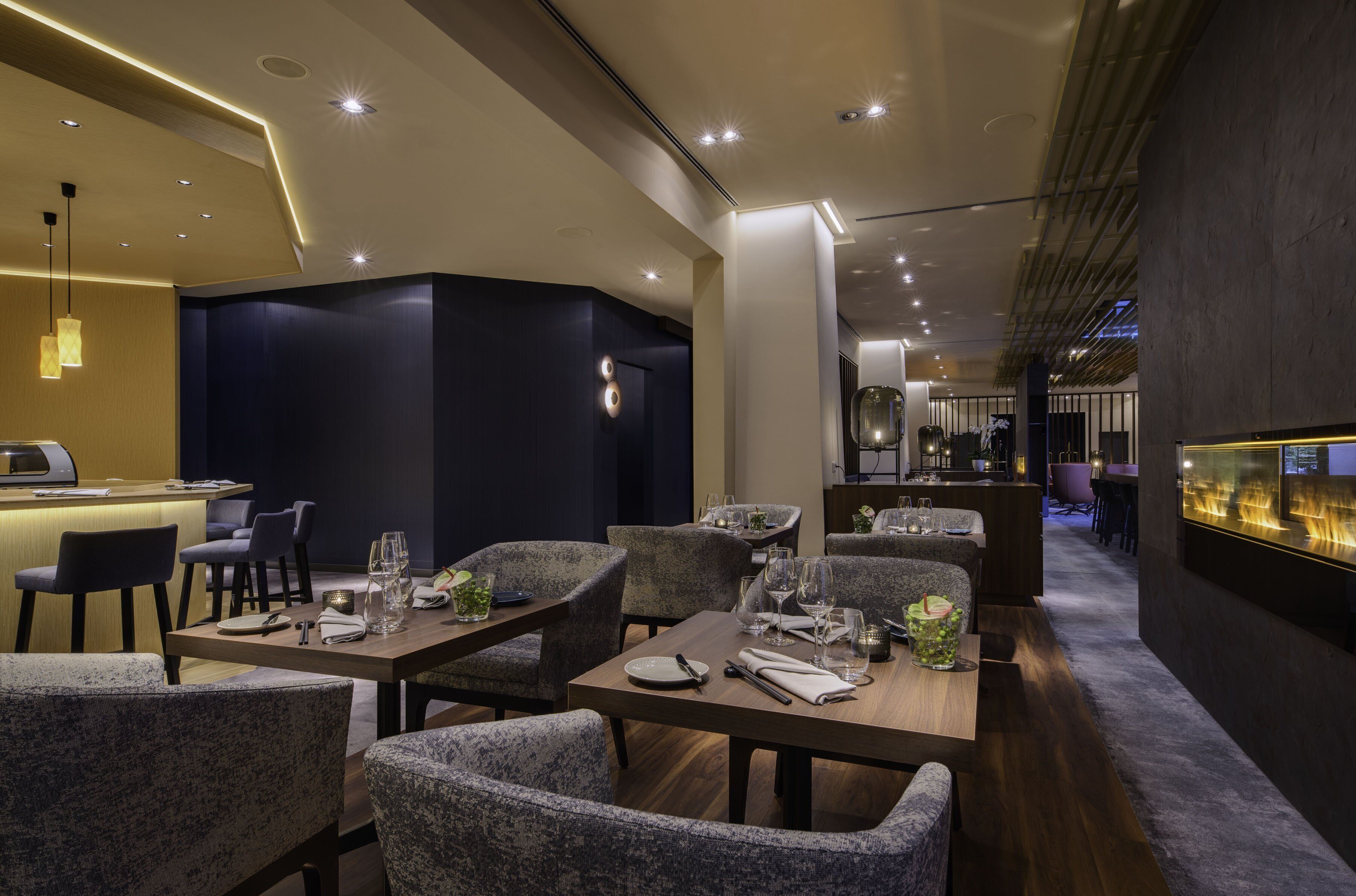 Un restaurante moderno con una pared de acento azul oscuro, mesas de madera y sillas tapizadas en gris.