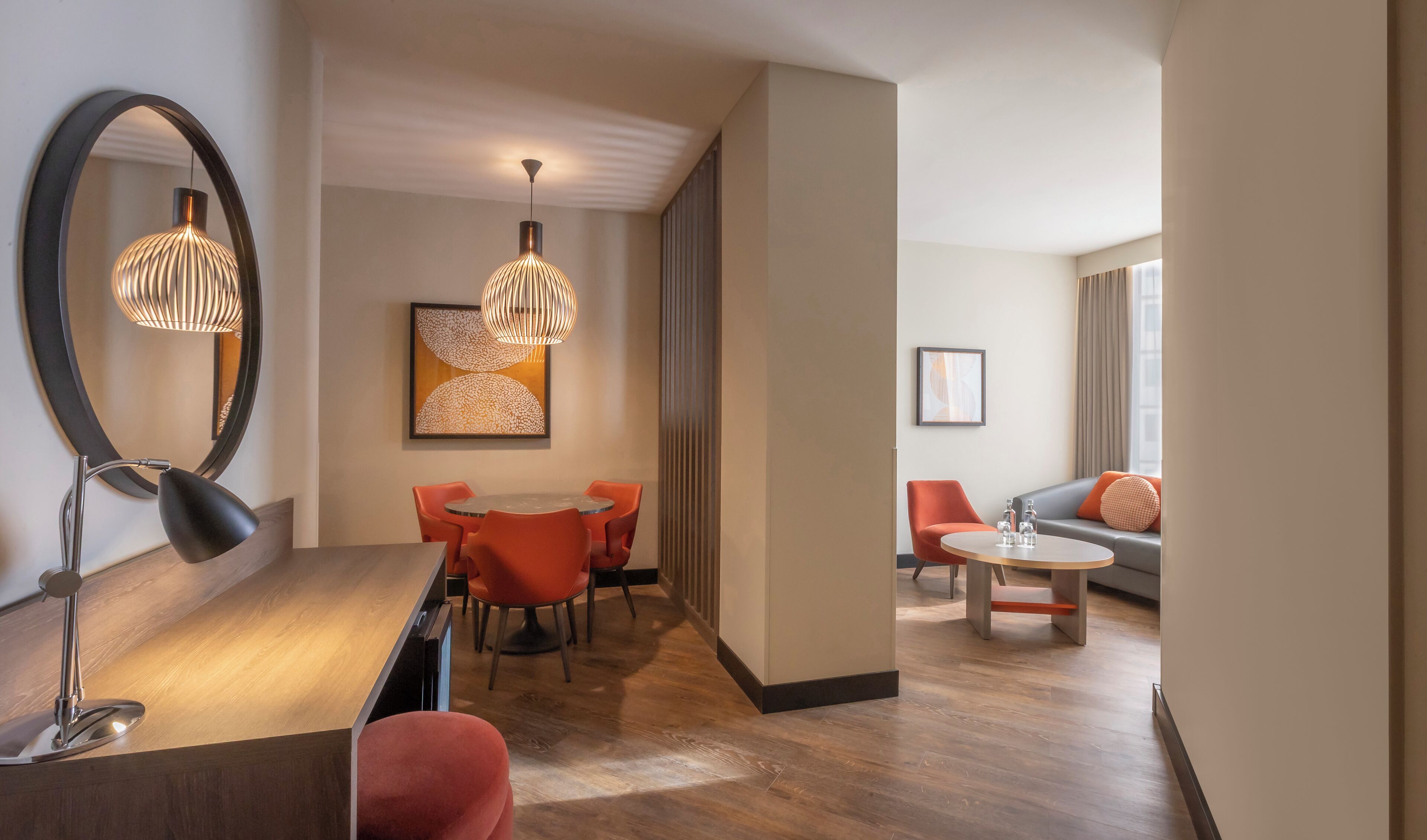 A modern hotel room with a dining area, a sofa, and a large mirror.
