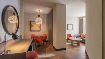 Una habitación de hotel moderna con zona de comedor, sofá y un espejo grande.