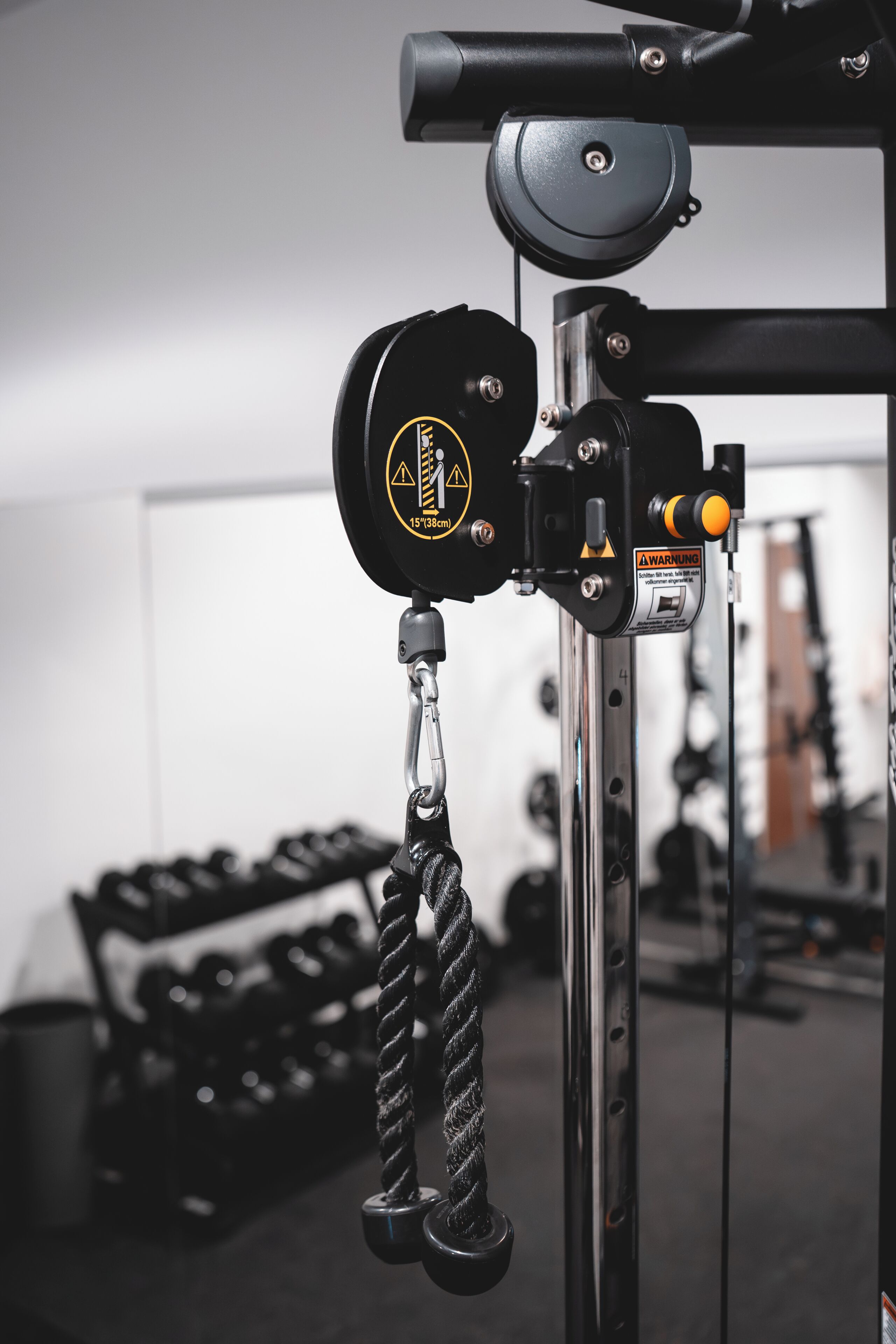 A gym equipment setup with a cable machine, weight stack, and a warning label.