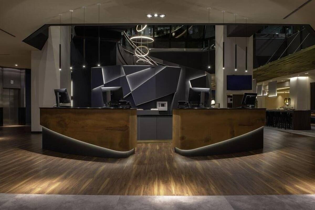 Un área de recepción moderna con un mostrador curvo, una gran lámpara abstracta y una escalera al fondo.