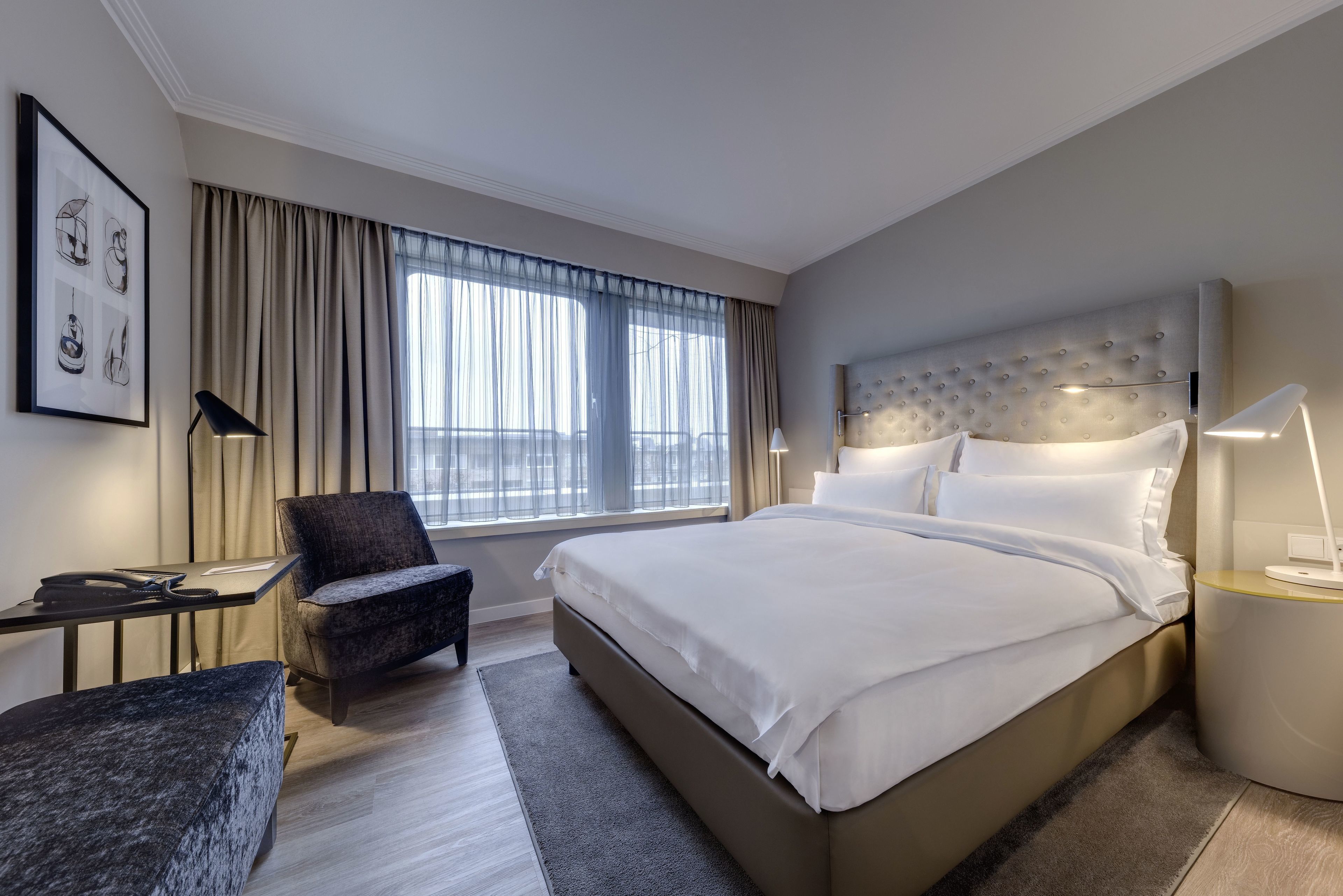 Een moderne hotelkamer met een groot bed, een bureau, een stoel en een raam met gordijnen.
