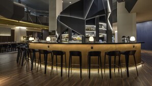 Zona de bar moderna con una barra central, taburetes y una variedad de botellas y vasos.