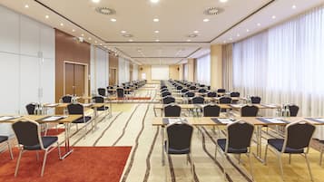 A conference room with rows of tables and chairs, a projector screen, and a large window with curtains.