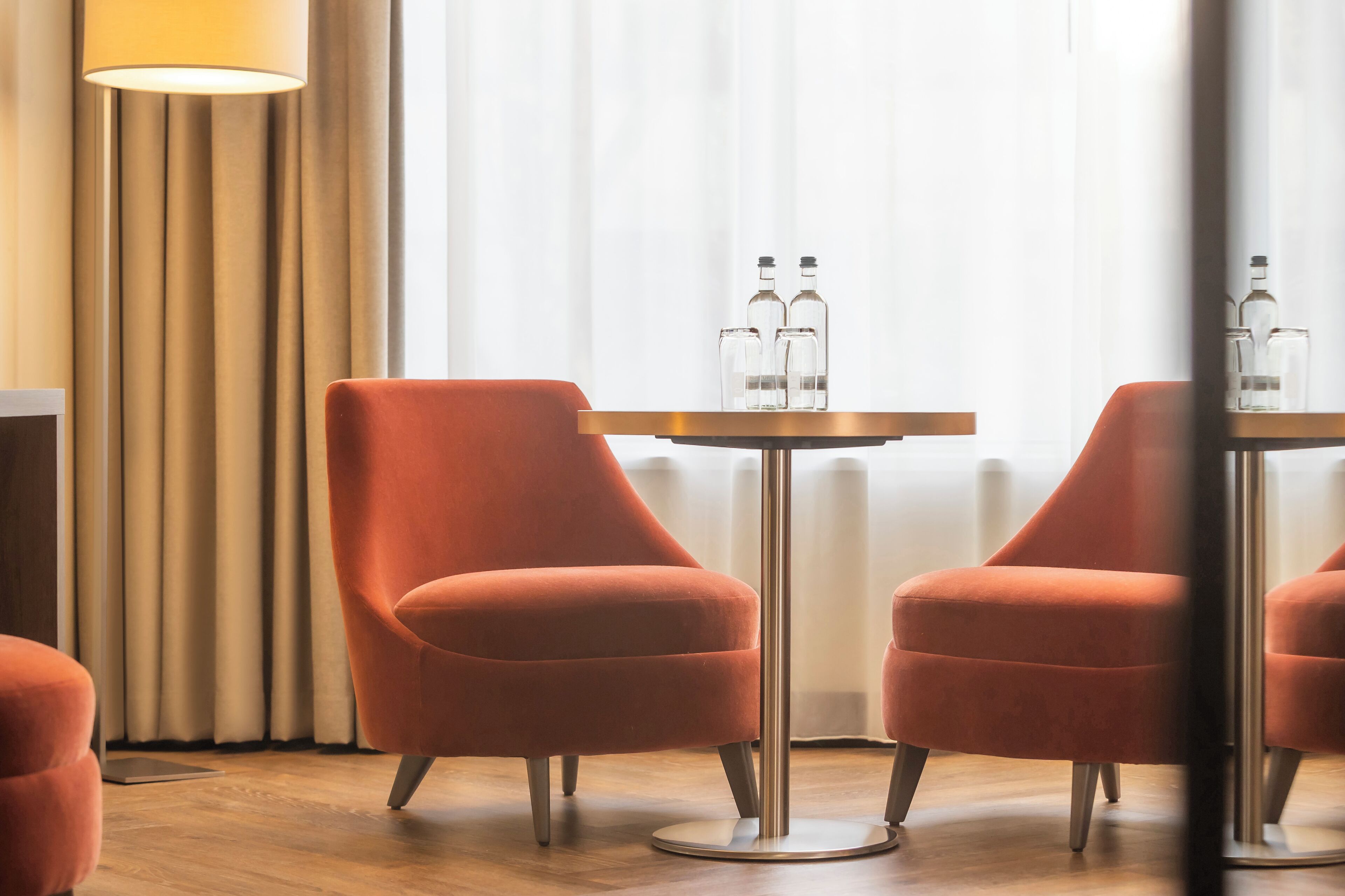 Una habitación moderna con dos sillones anaranjados, una mesa redonda con dos botellas, una lámpara de pie y un radiador.
