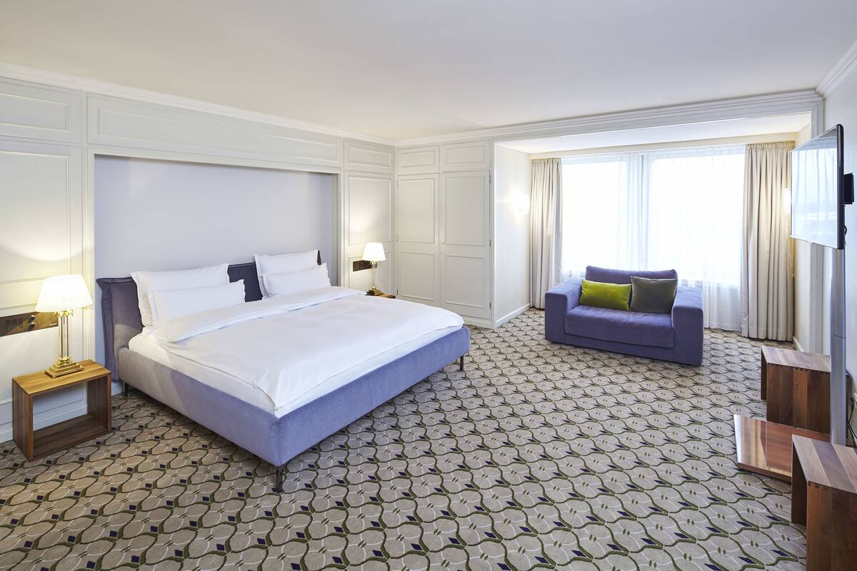 Una habitación de hotel con una cama grande, un sofá, un televisor y una alfombra estampada.