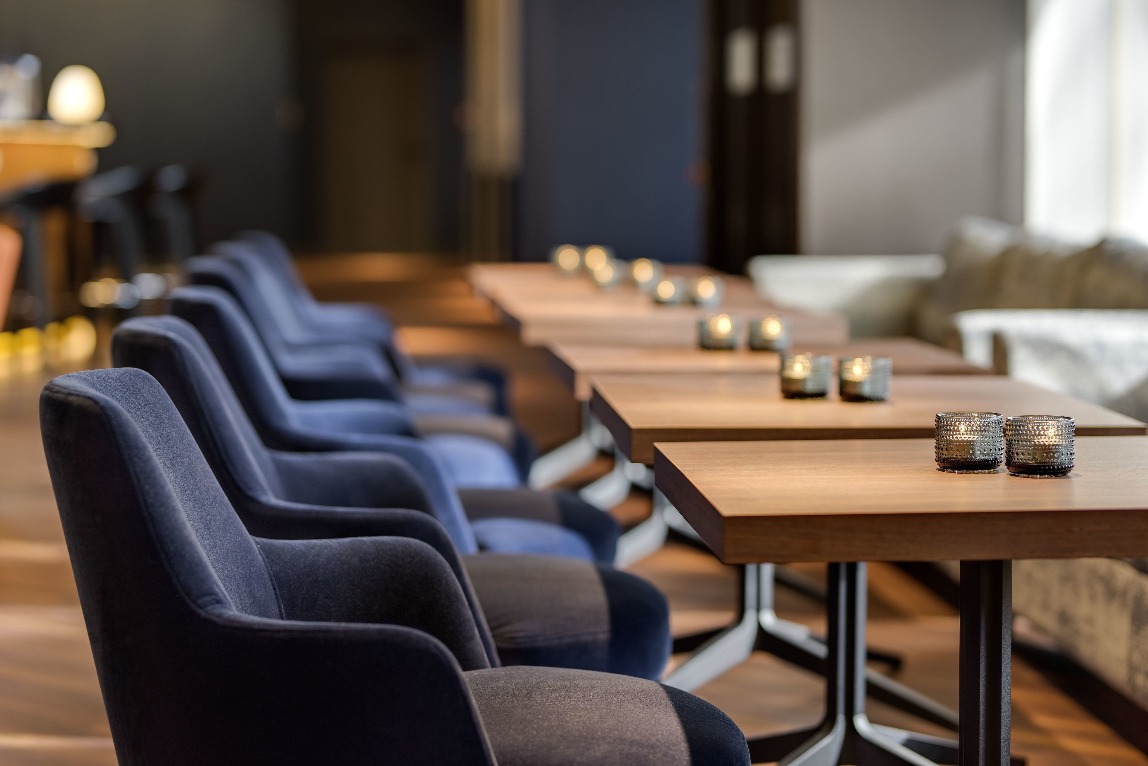 Une rangée de chaises bleu foncé et de tables en bois, agrémentées de bougies, créant une ambiance chaleureuse et invitante.