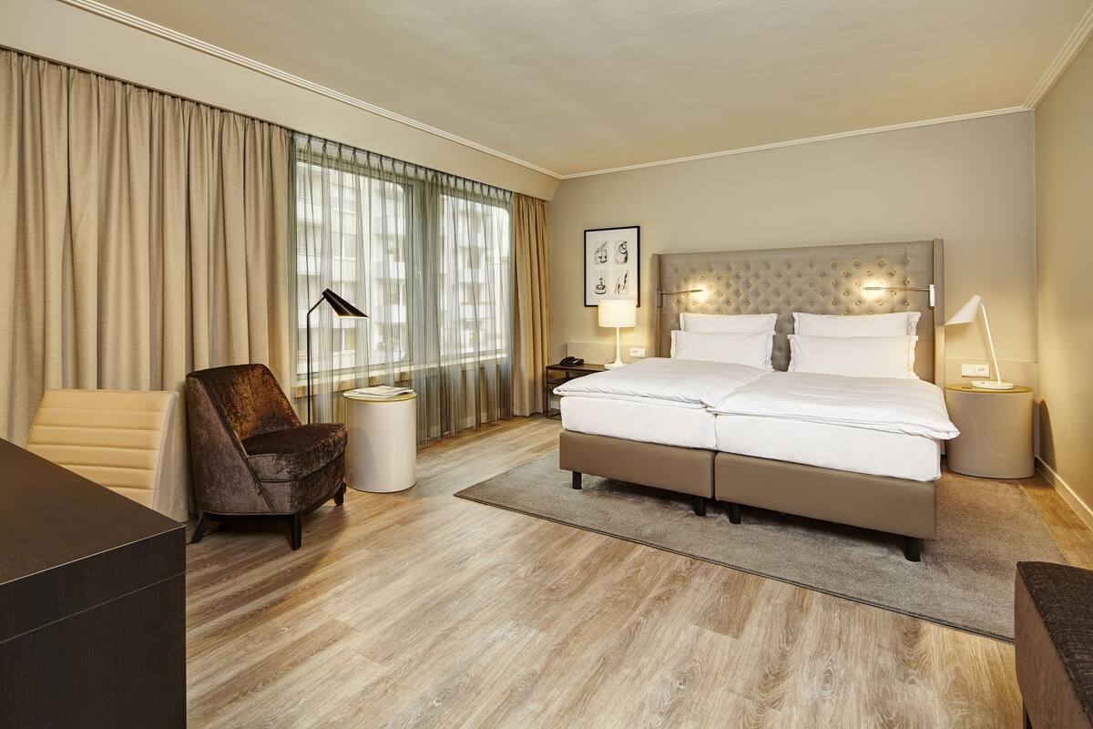 Una habitación de hotel con una cama grande, una silla, un escritorio y una ventana con cortinas.